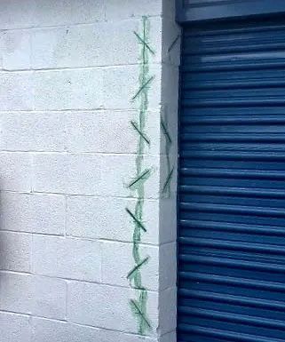 Gray cinder block wall with green stitches along a crack next to a blue metal door.