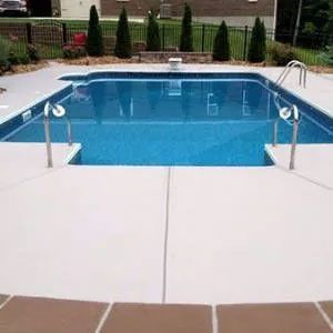 Swimming pool with blue water and white concrete deck, surrounded by landscaping.