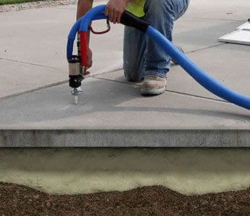 Man kneeling, using a machine to inject foam under a concrete slab for leveling. Blue hose, tan foam.