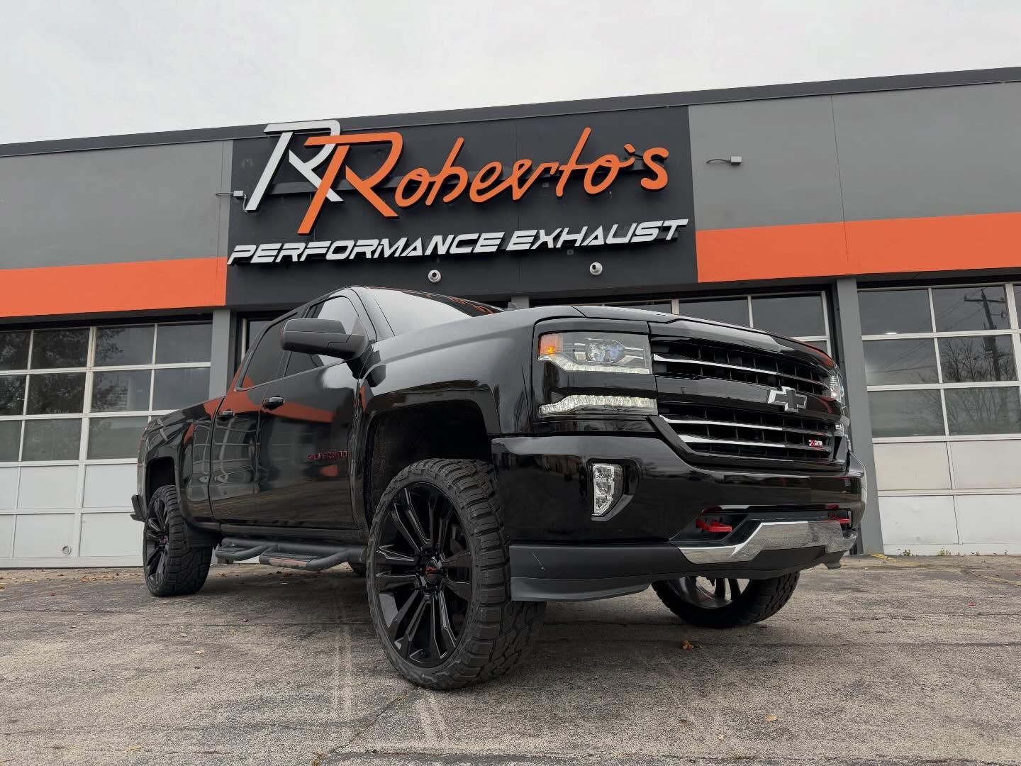 A black Chevrolet pickup truck parked in front of a building sign for Roberto's Performance Exhaust.