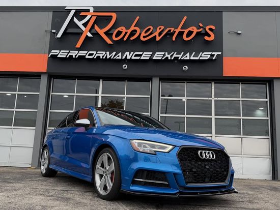 A blue Audi parked in front of a building with a Roberto’s Performance Exhaust sign.