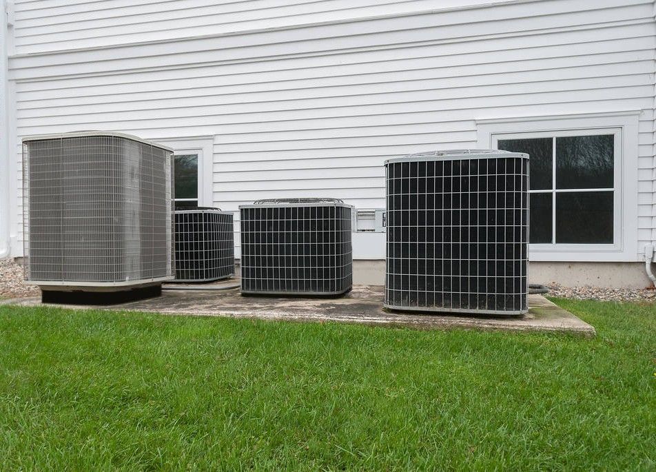 Four air conditioning units on a concrete pad near a white-sided building and grass.