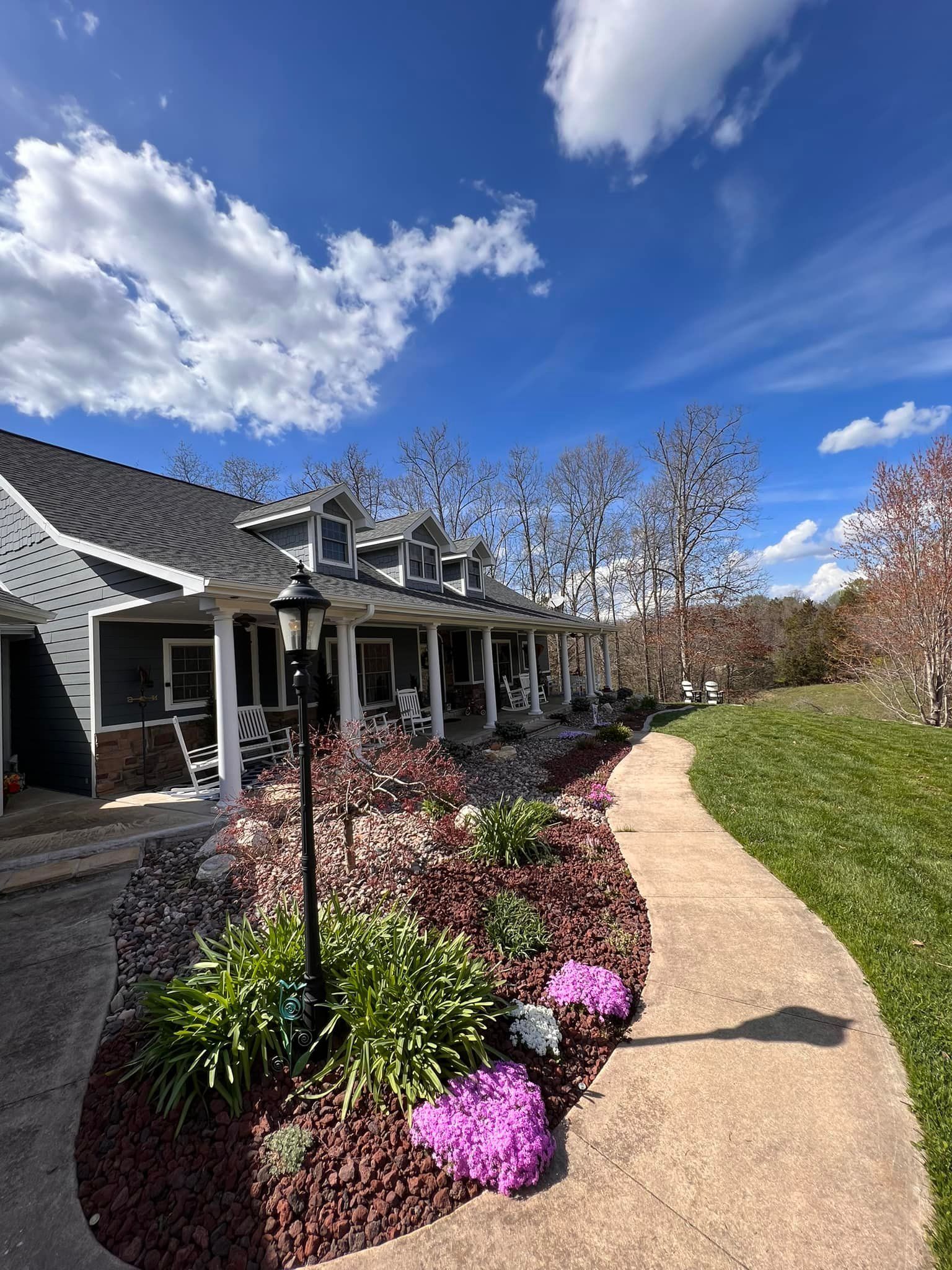 A house with a porch, a walkway, and colorful flower beds under a bright blue sky.