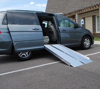 A van with a ramp attached to it is parked in a parking lot.