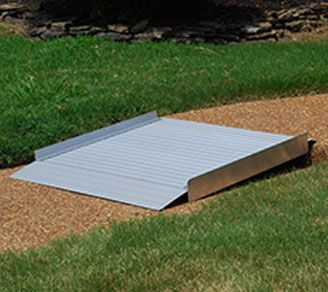 A metal ramp is sitting on top of a dirt path in the grass.