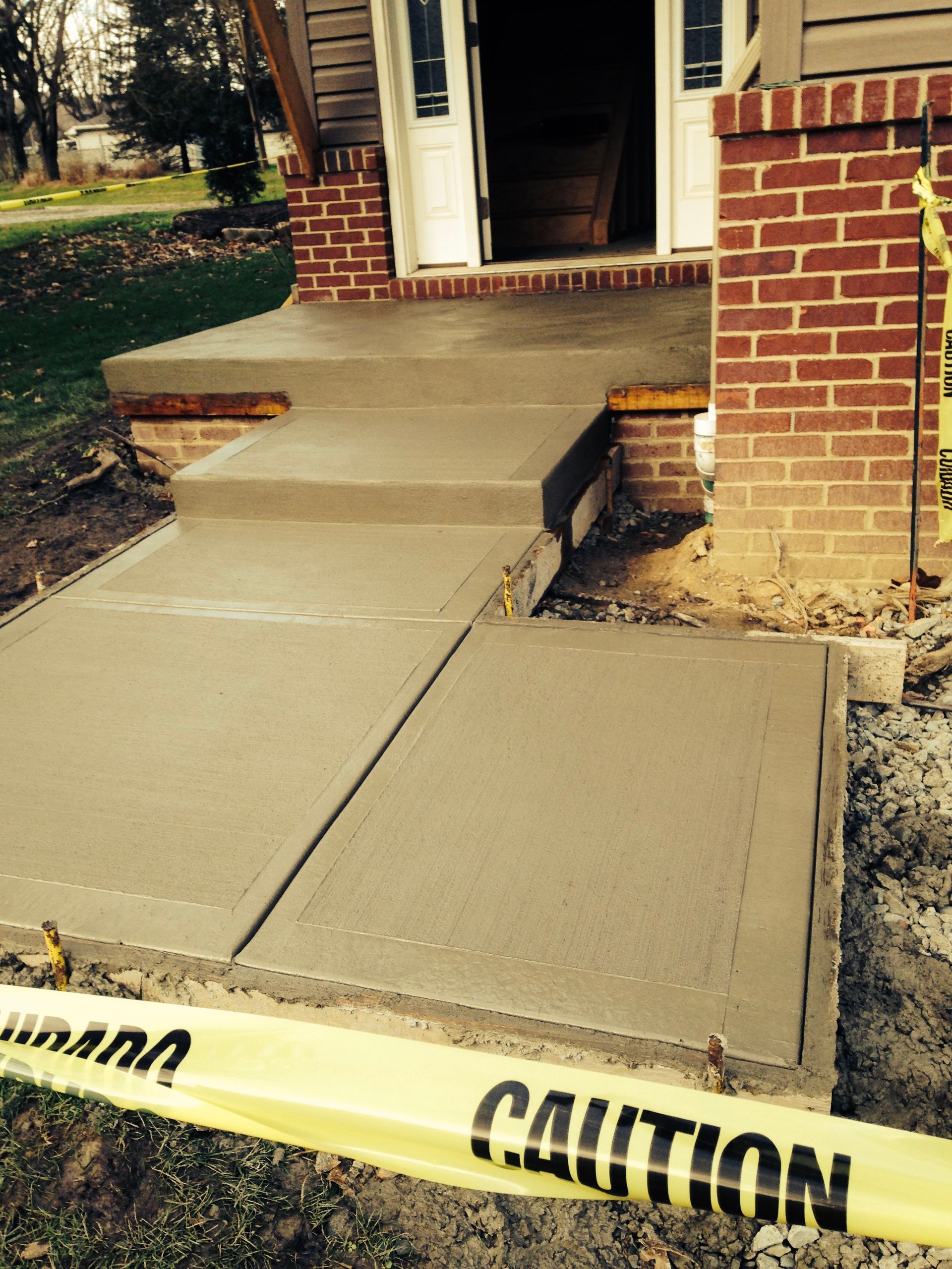 Damaged concrete walkway and ramp at a brick building entrance, marked with caution tape