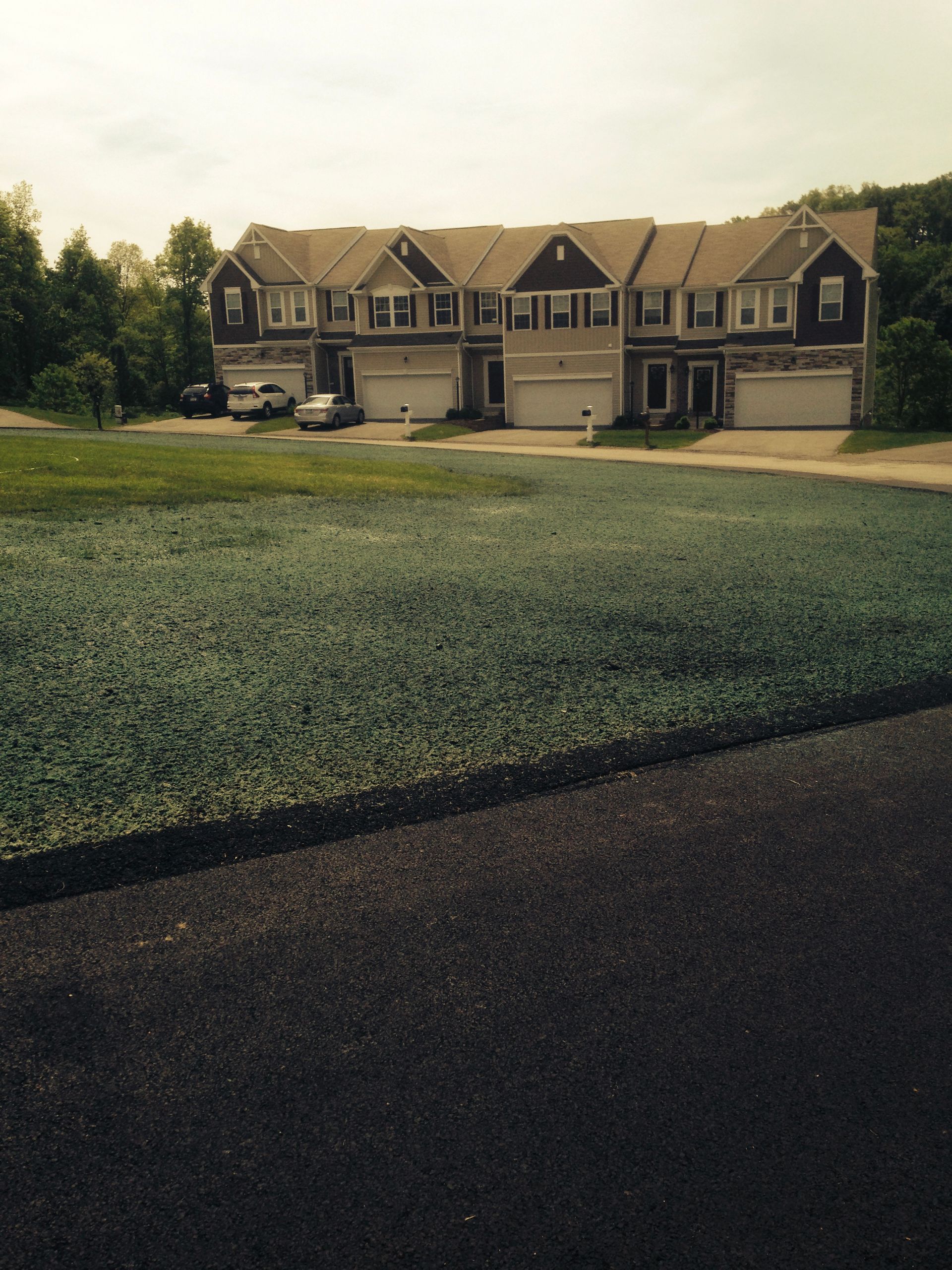 Suburban row of beige townhouses beside a wide green lawn at dusk