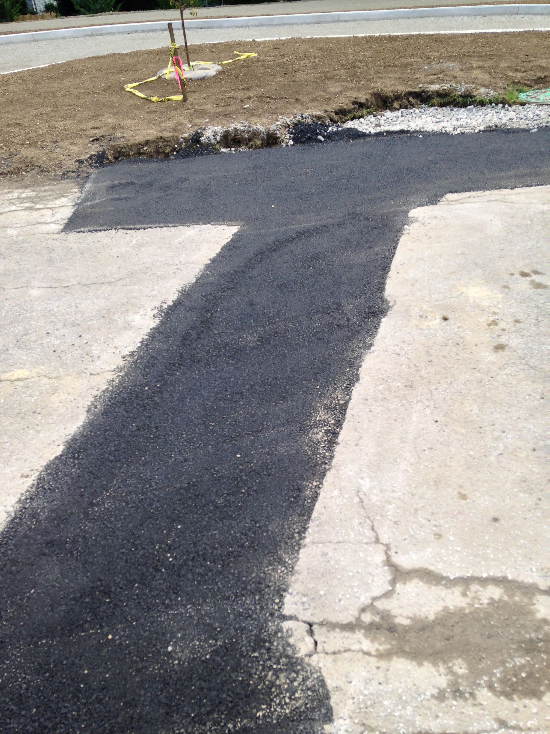 Black asphalt repair patch over a cracked concrete driveway near a curb and mulch bed