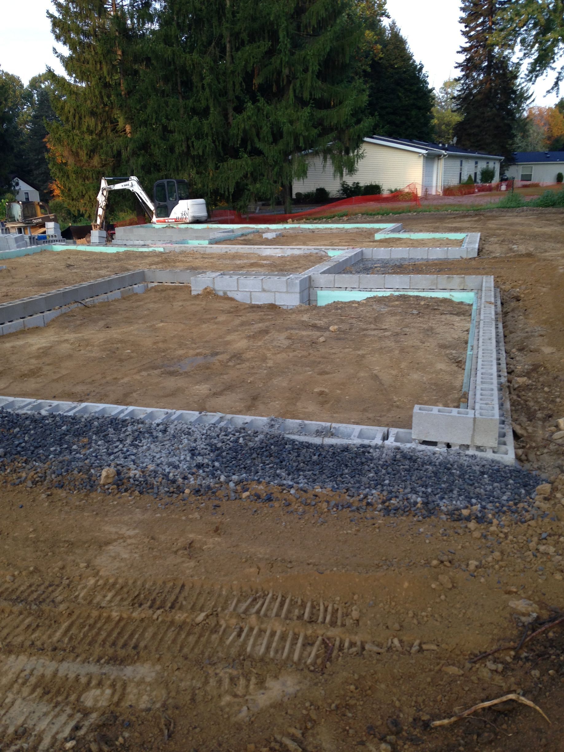 Construction site with gravel foundation footings and excavator in the background