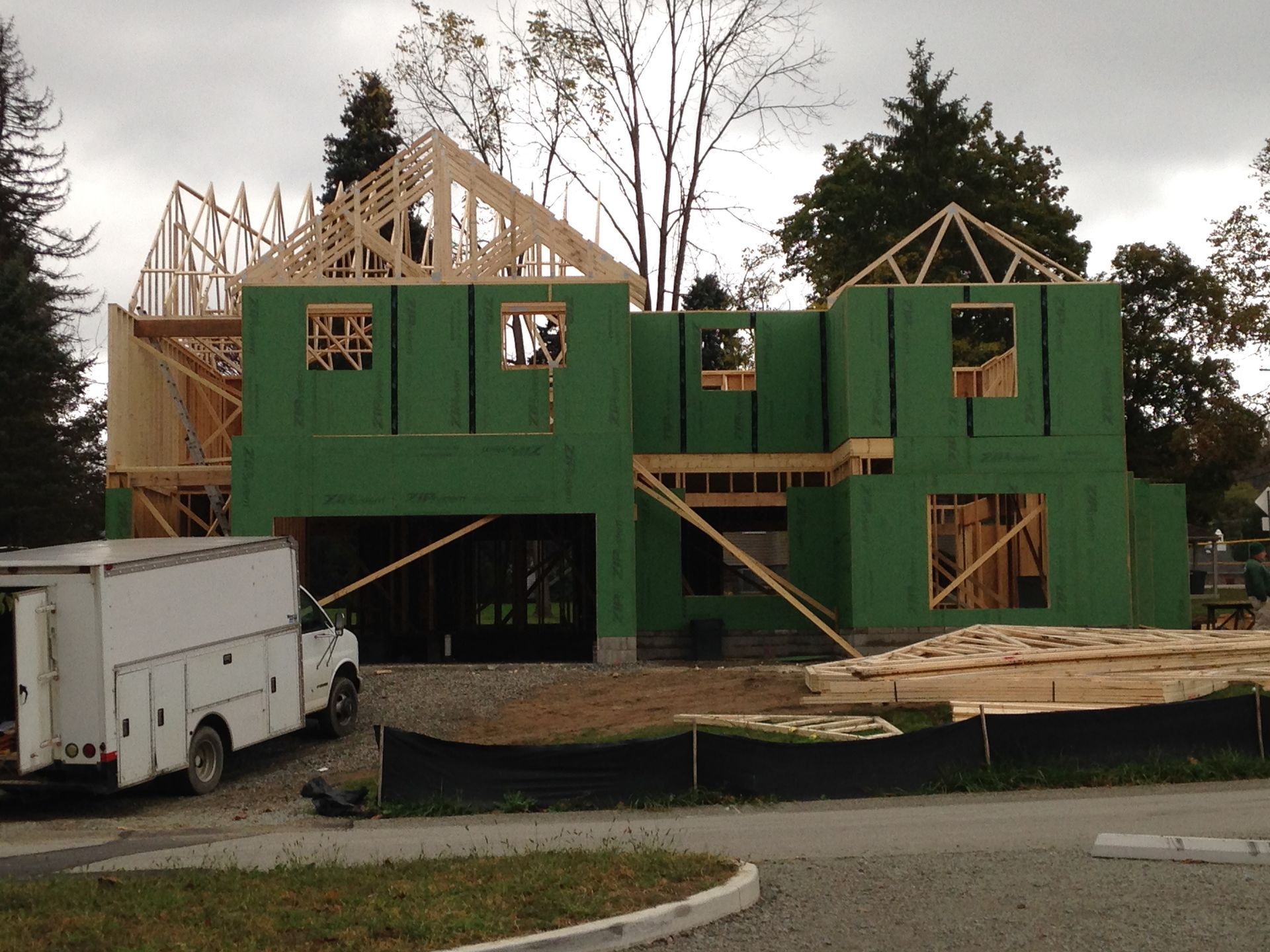 House under construction with green sheathing, exposed roof framing, and a white truck nearby