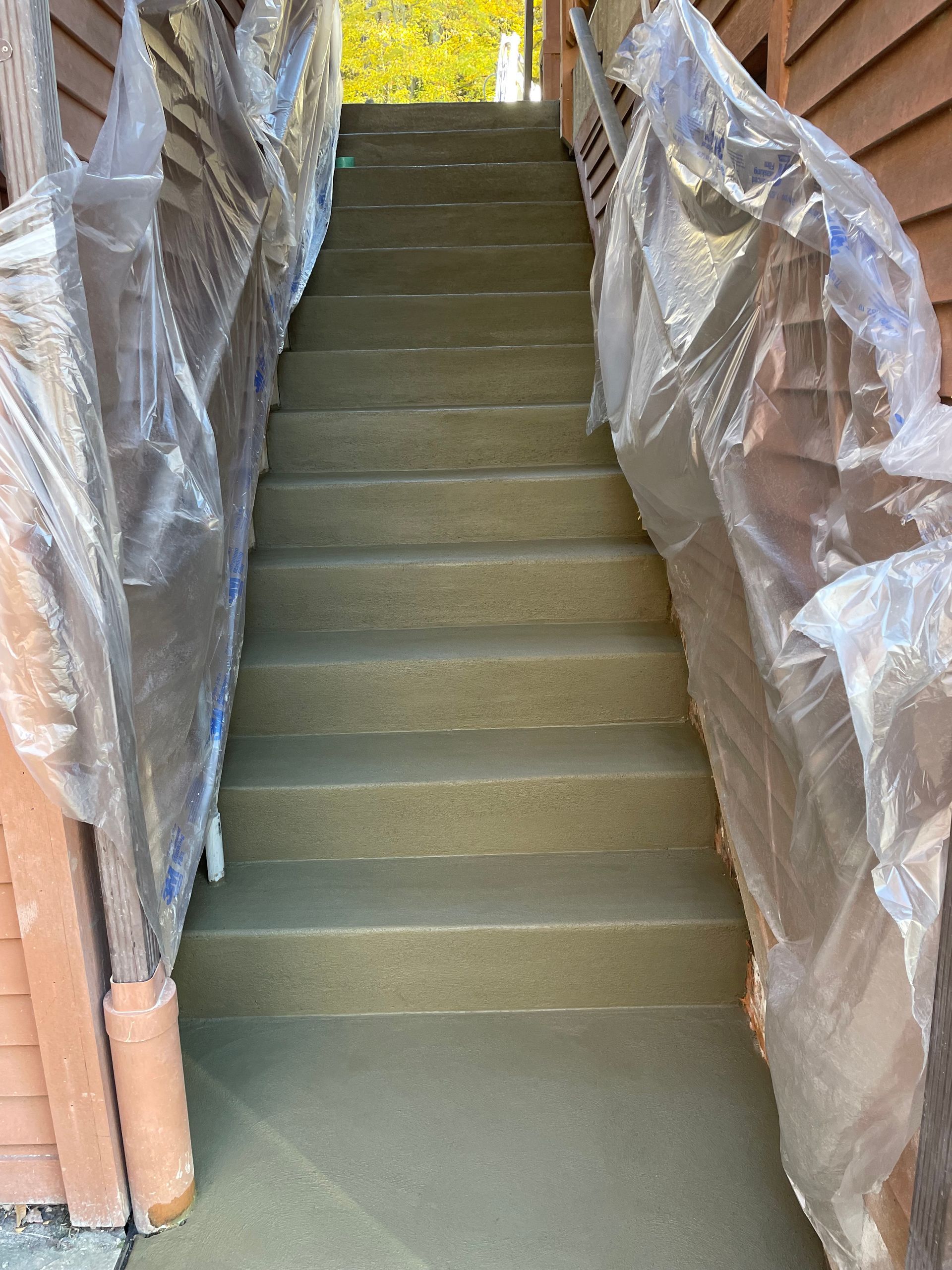 Staircase under construction, wrapped in plastic sheeting on both sides, leading upward to daylight
