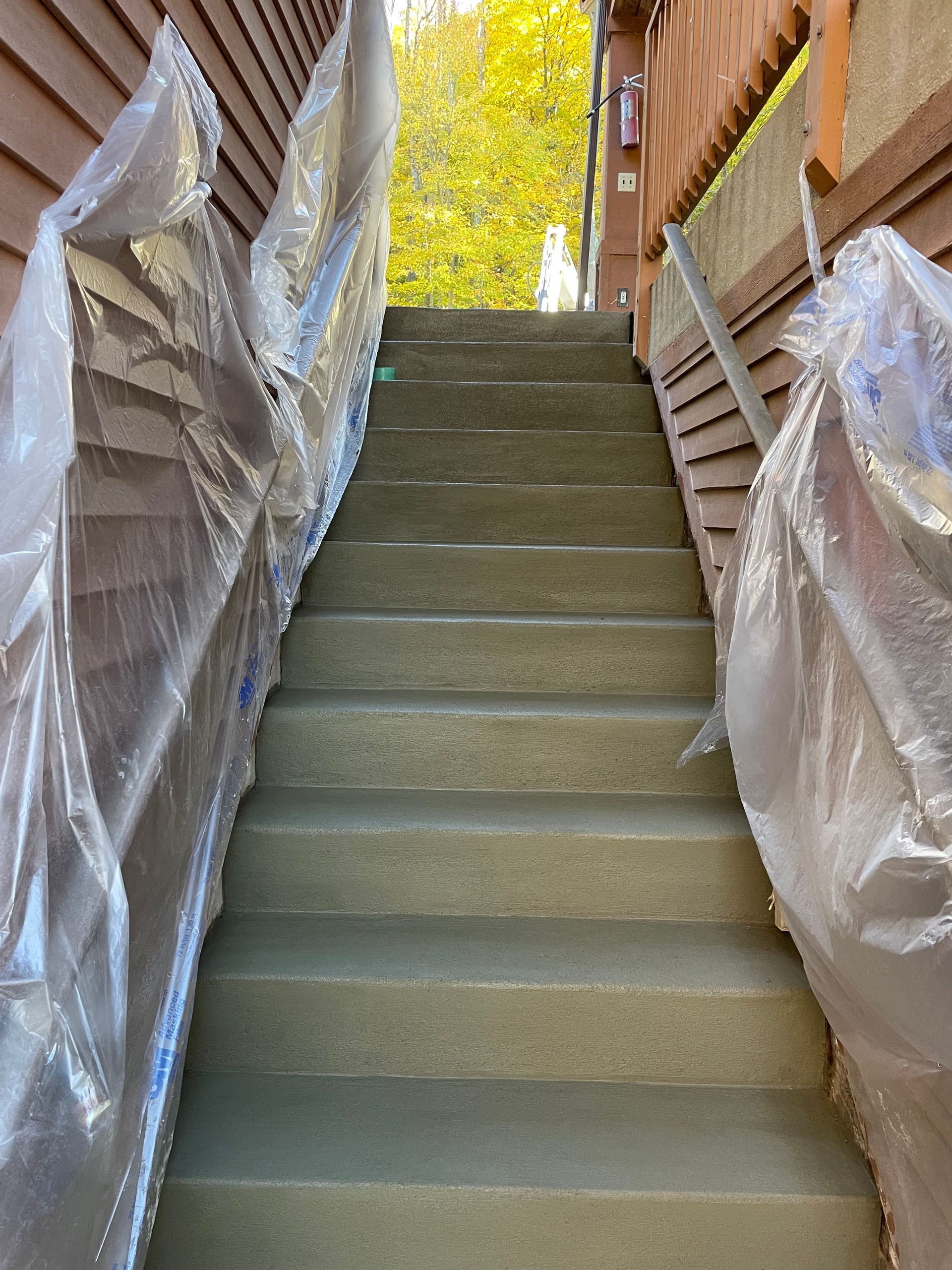 Staircase between wrapped building materials, leading up outdoors toward bright yellow trees.