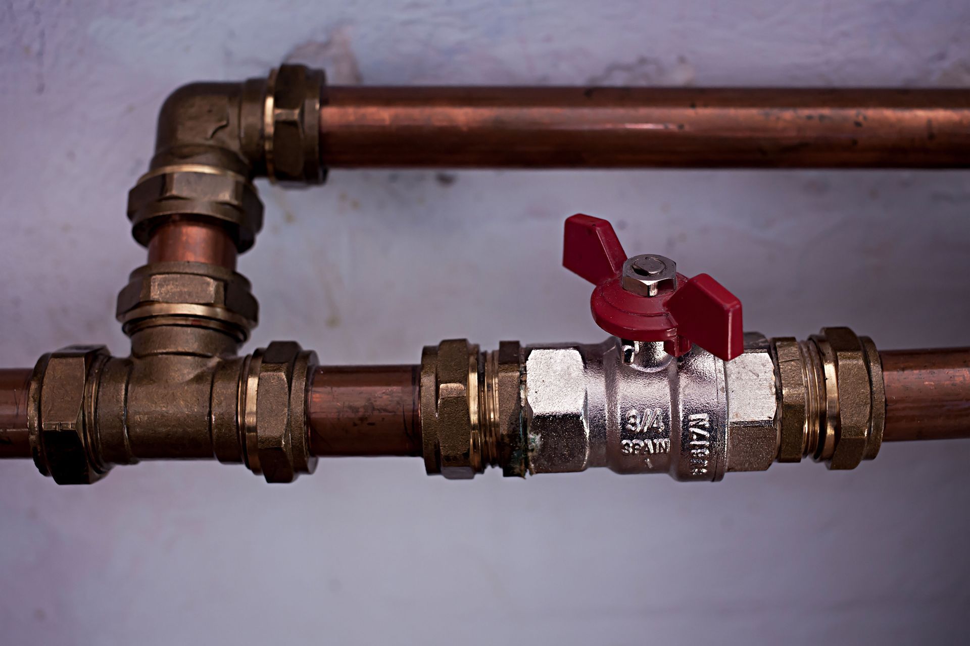 Copper pipes with a red-handled shutoff valve on a wall