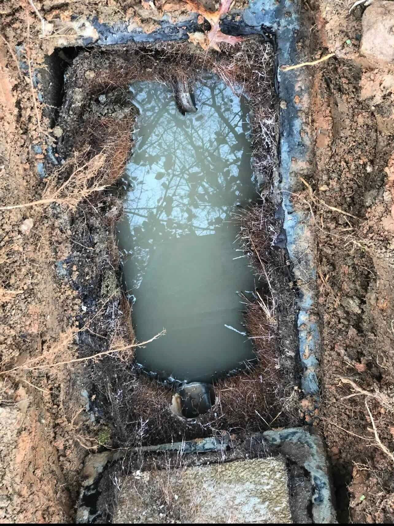 Mud-filled rectangular trench or utility hole with standing water in a dirt excavation area
