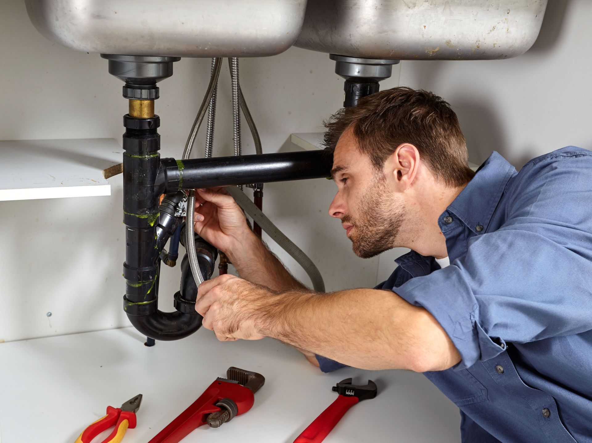 Plumber repairing pipes under a kitchen sink with tools on the floor