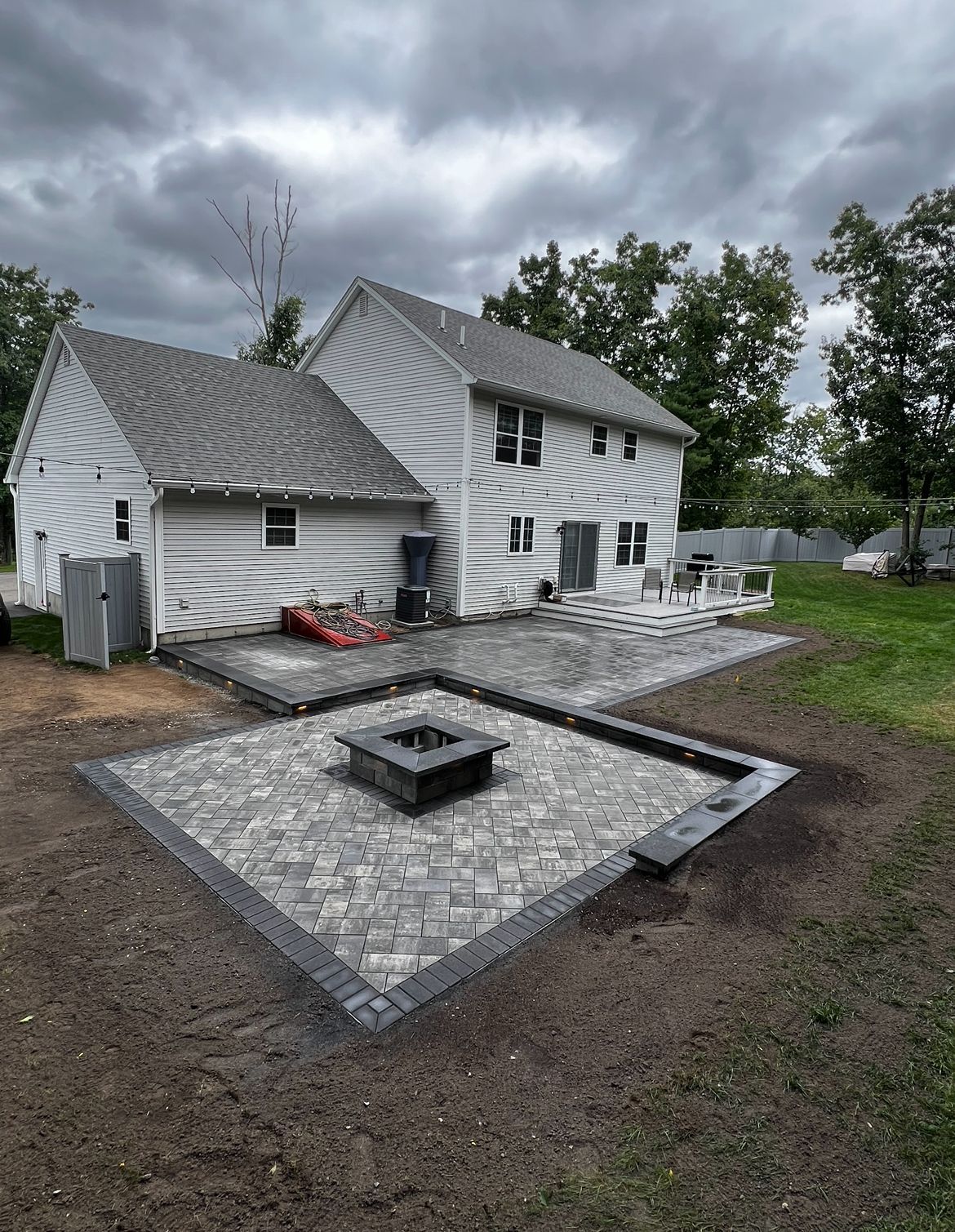 A light-colored two-story house with a new gray stone patio and square fire pit in the backyard.