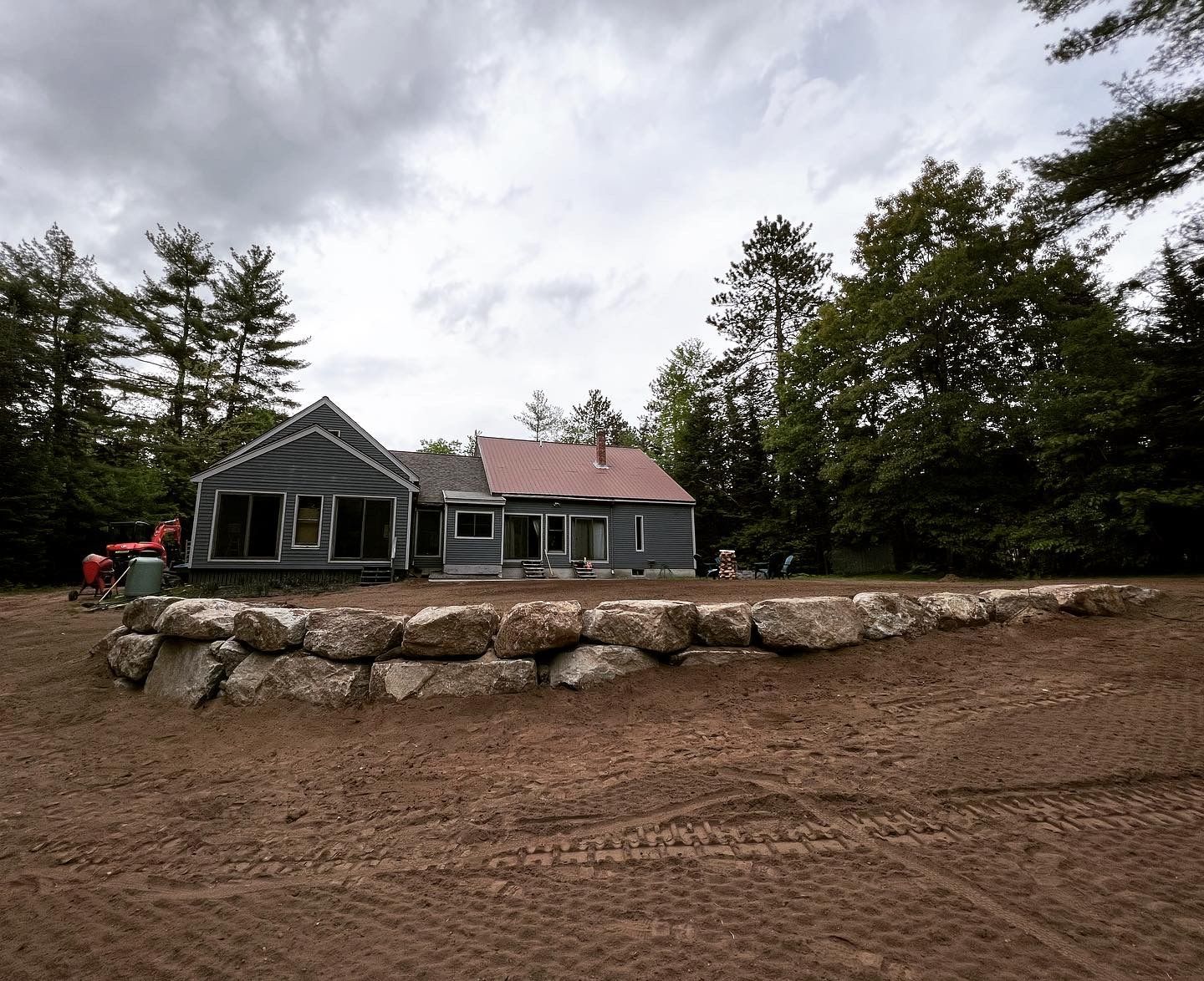 A stone retaining wall sits in front of a house under renovation, set against a backdrop of trees and a cloudy sky.