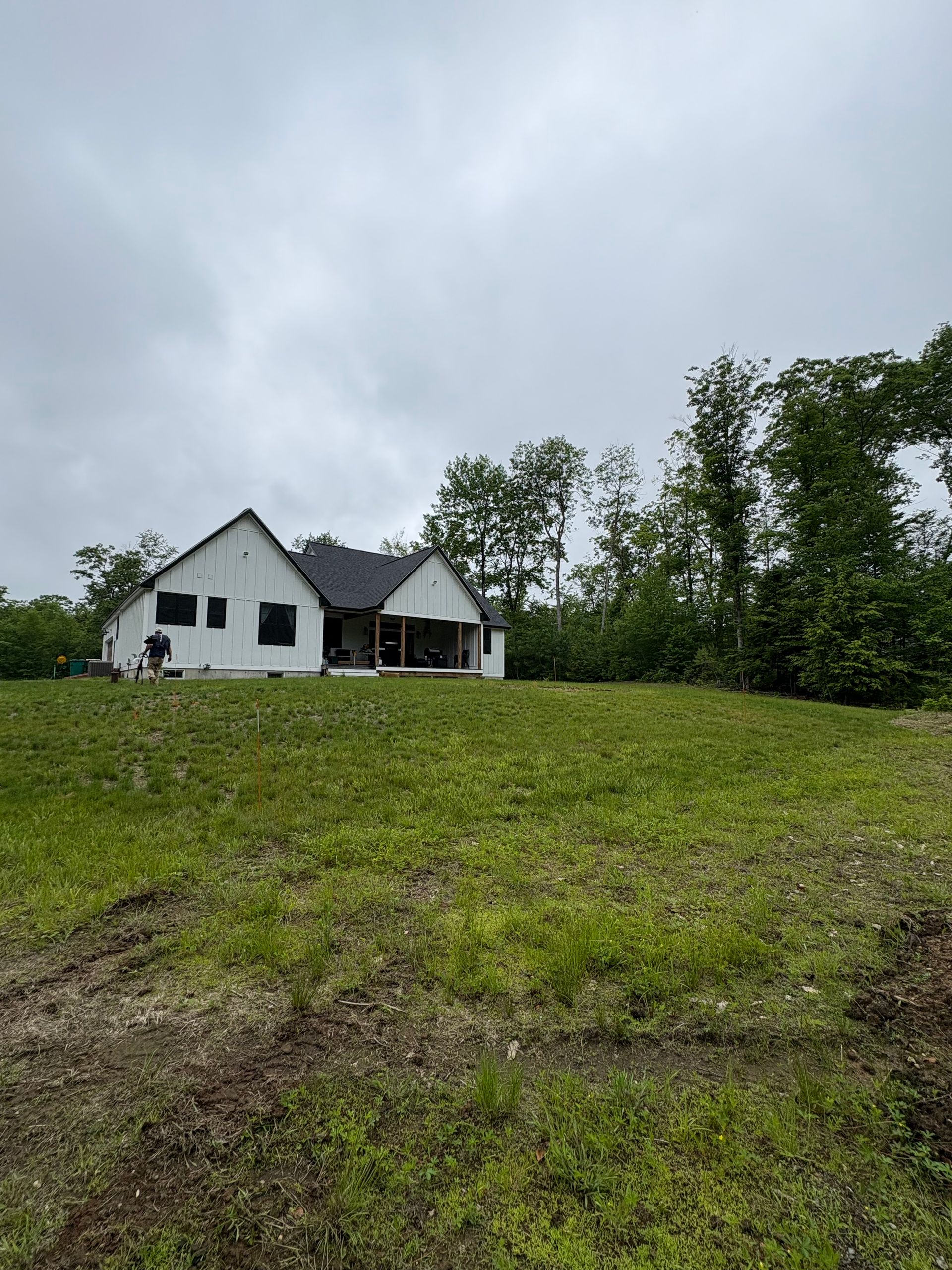 A white house under construction with a dark roof sits on a grassy hill under a cloudy sky.
