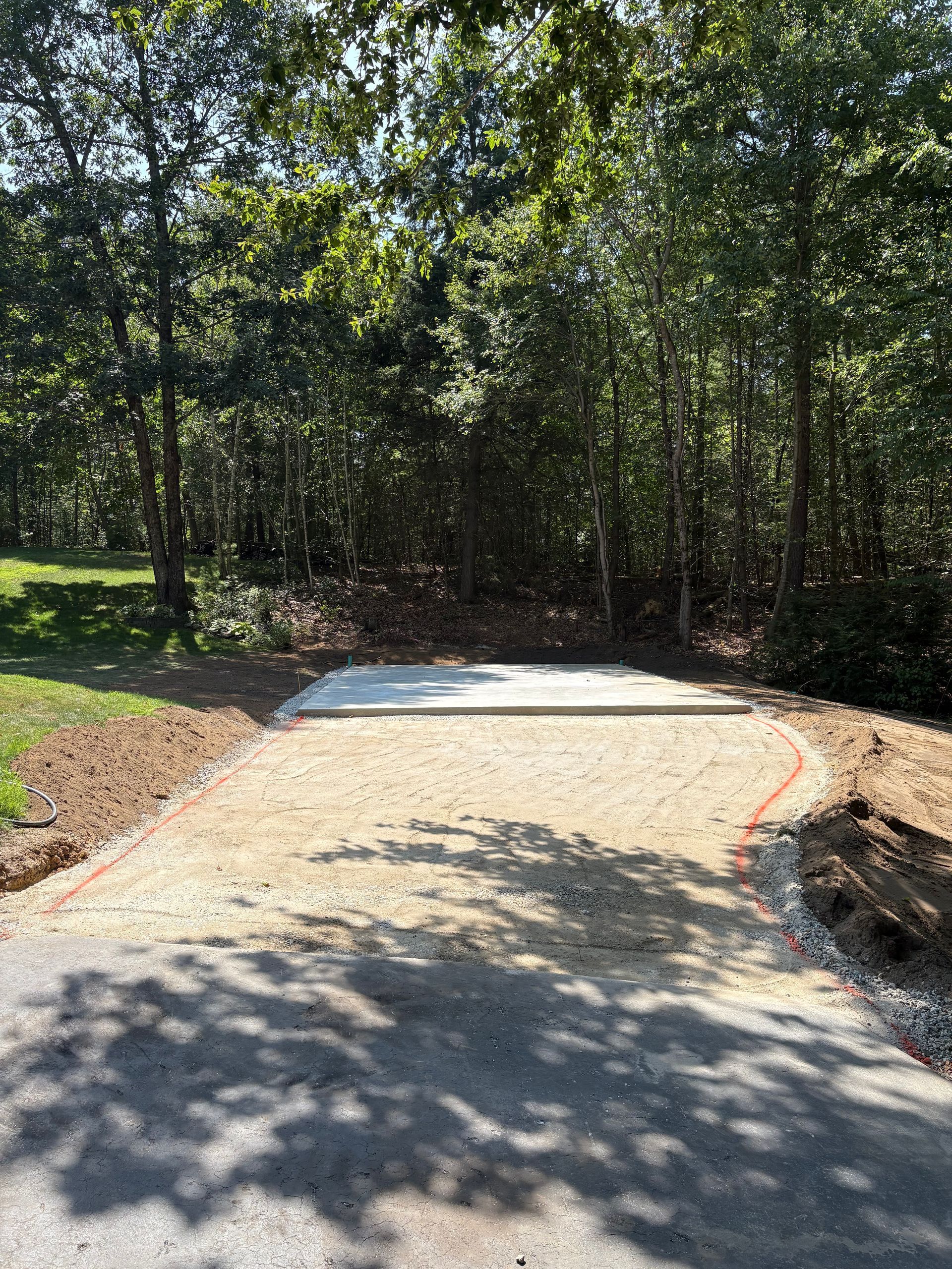 A gravel driveway leads to a concrete pad situated at the edge of a lush, wooded forest.