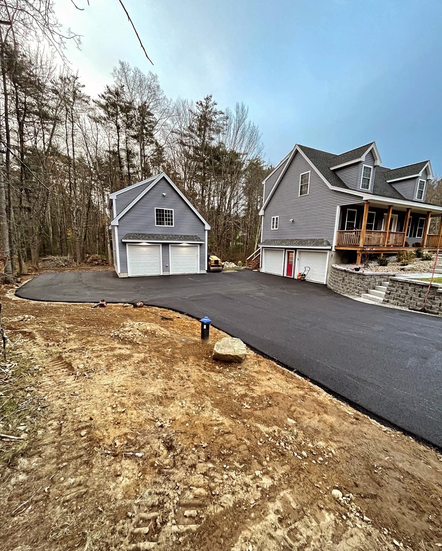 A paved driveway leads to a gray detached garage and a multi-story gray house nestled in a wooded area.