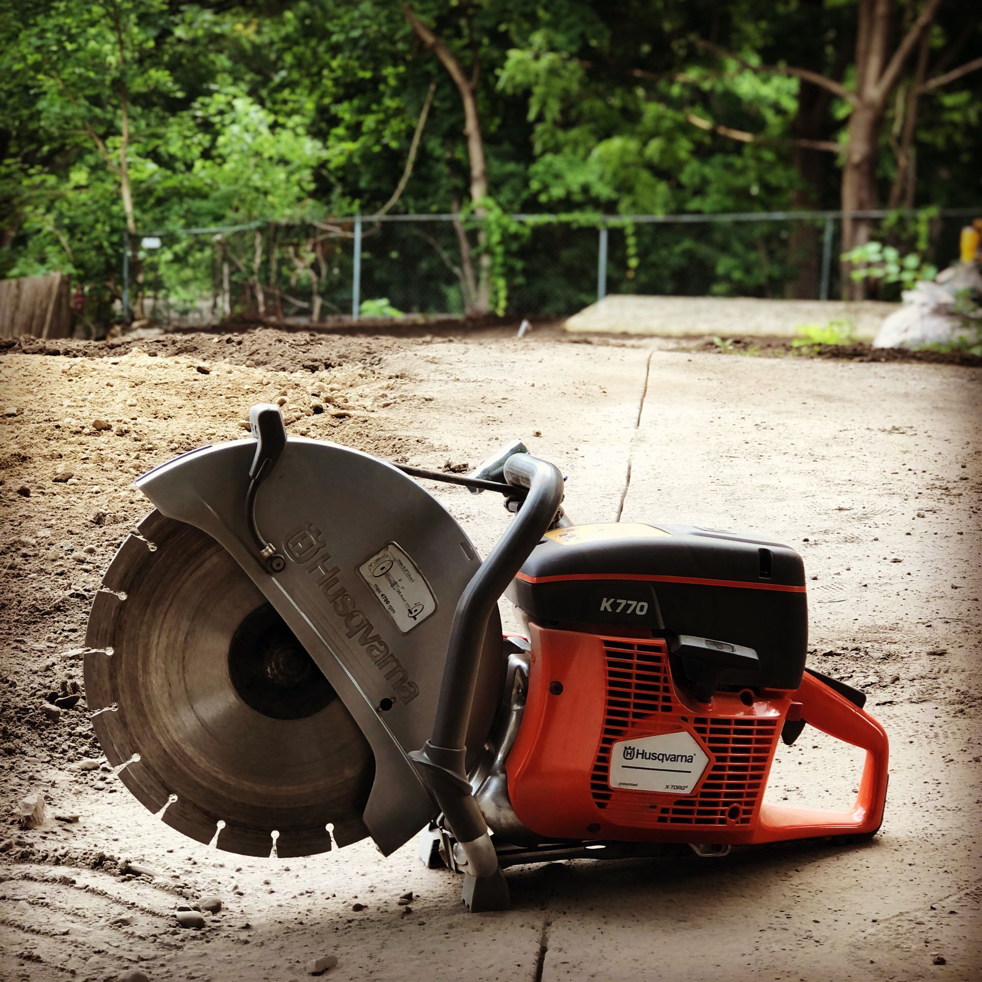 A bright orange Husqvarna K770 concrete saw resting on a dirt-covered concrete surface outdoors.