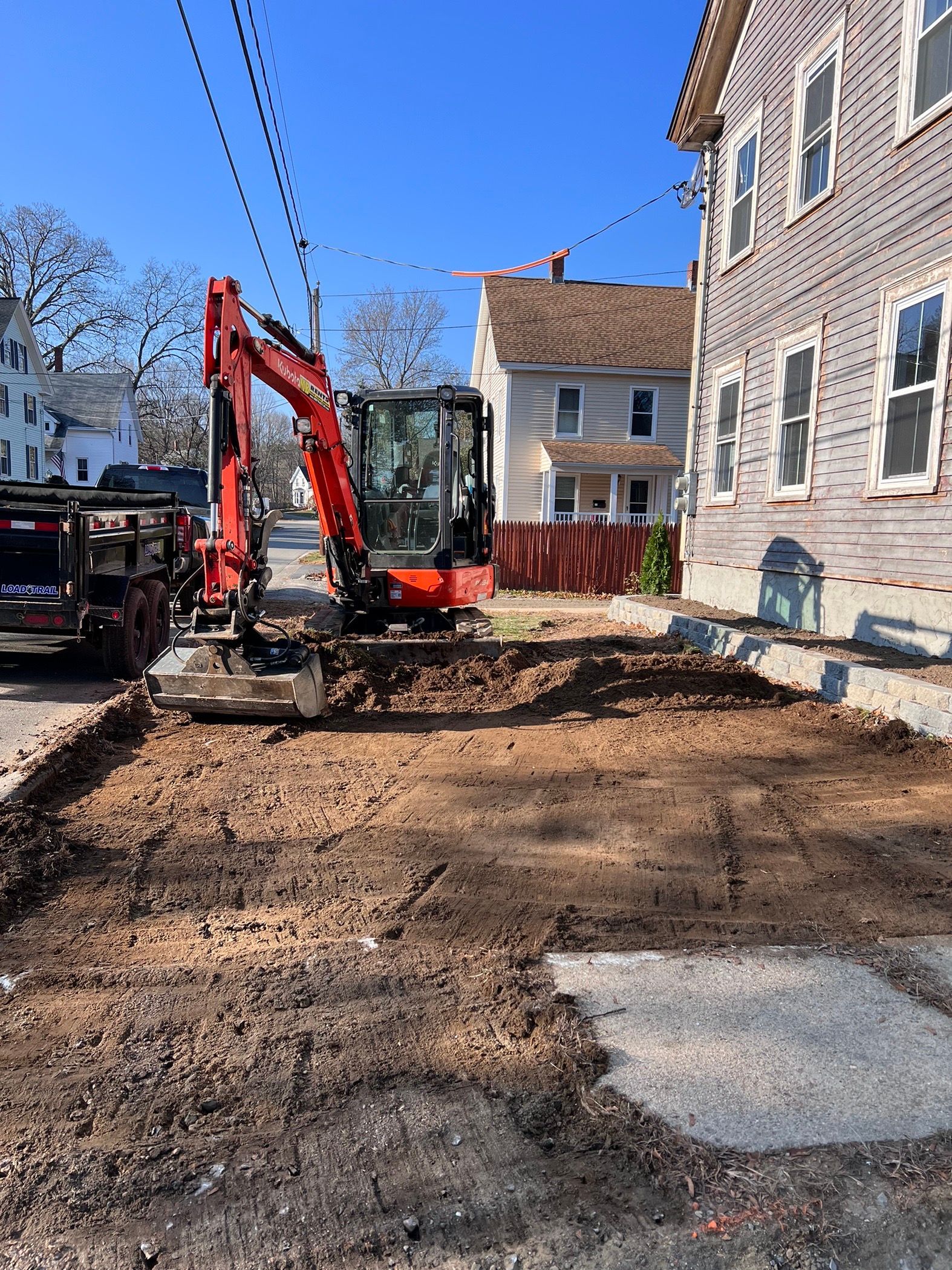 A red excavator parked on a construction site next to a house with exposed siding under a clear blue sky.