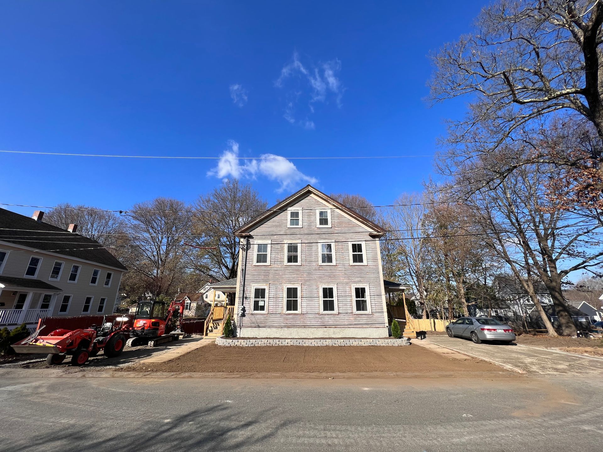 A light gray, three-story historic house with a new, rectangular gravel yard under a bright blue sky.