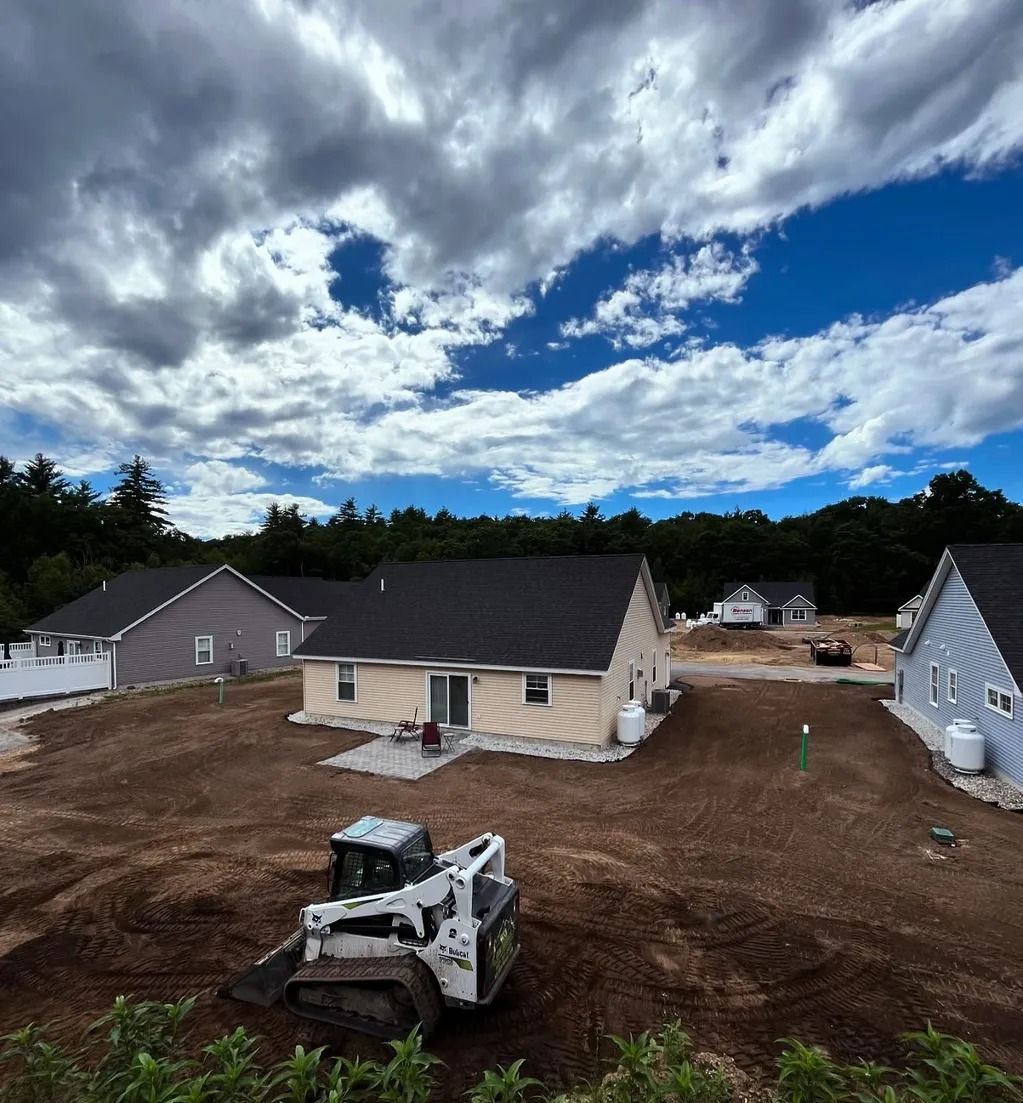 Construction site with houses, a skid steer, and a cloudy blue sky.