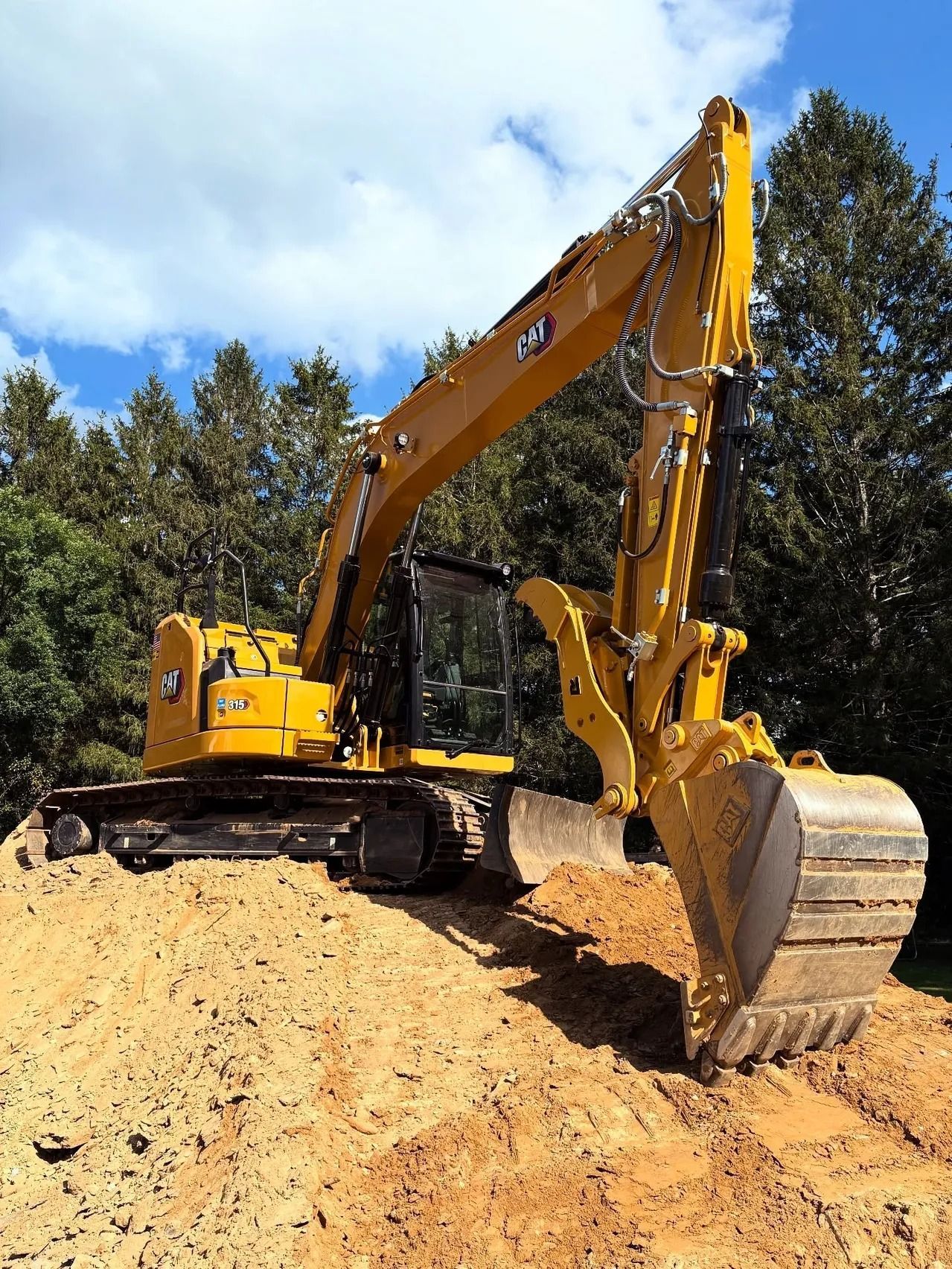 Yellow Caterpillar excavator digging in a dirt pile under a blue sky.