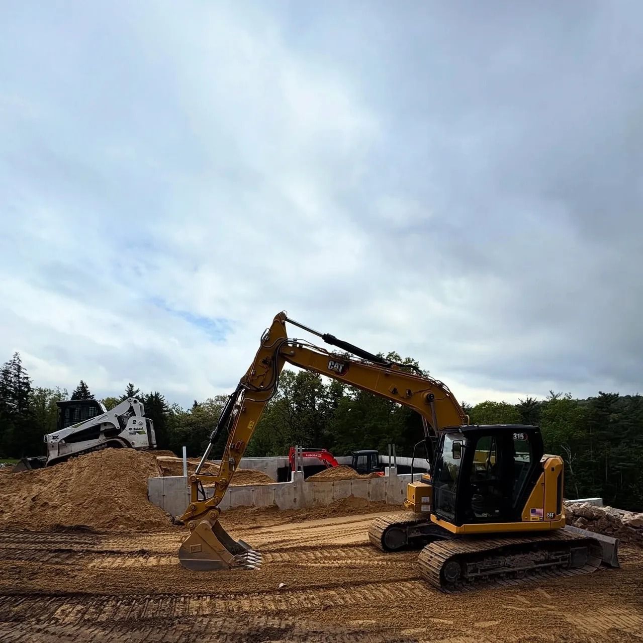 Yellow excavator at a construction site, preparing the foundation. Cloudy sky overhead.