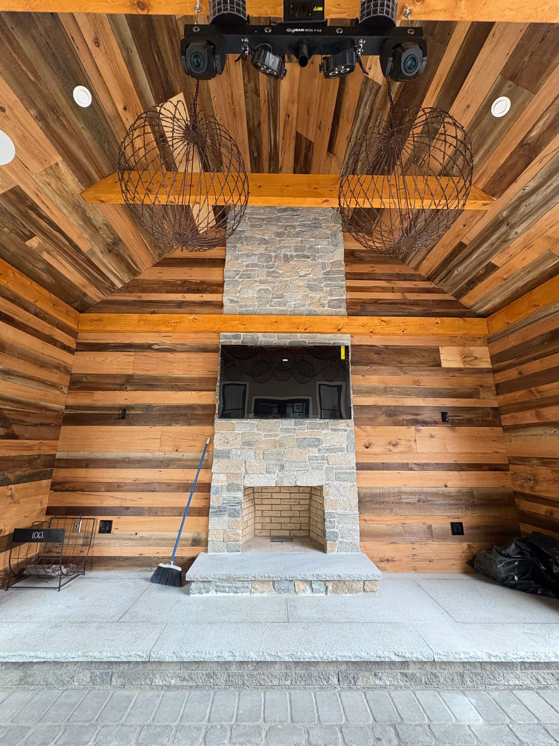 Rustic stone fireplace with a mounted television, centered on a wood-paneled wall inside a covered patio.