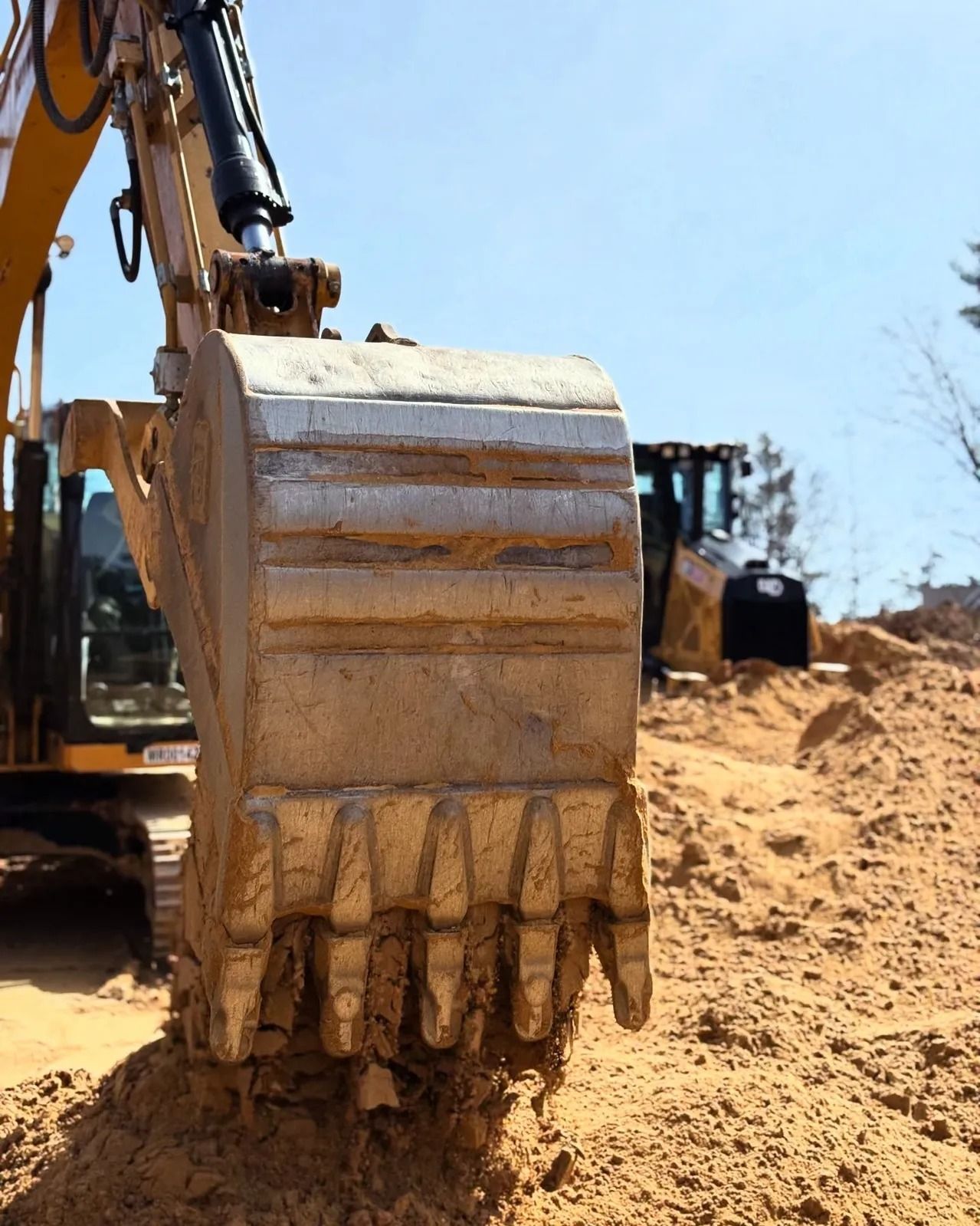 Excavator bucket scooping sand at a construction site on a sunny day.