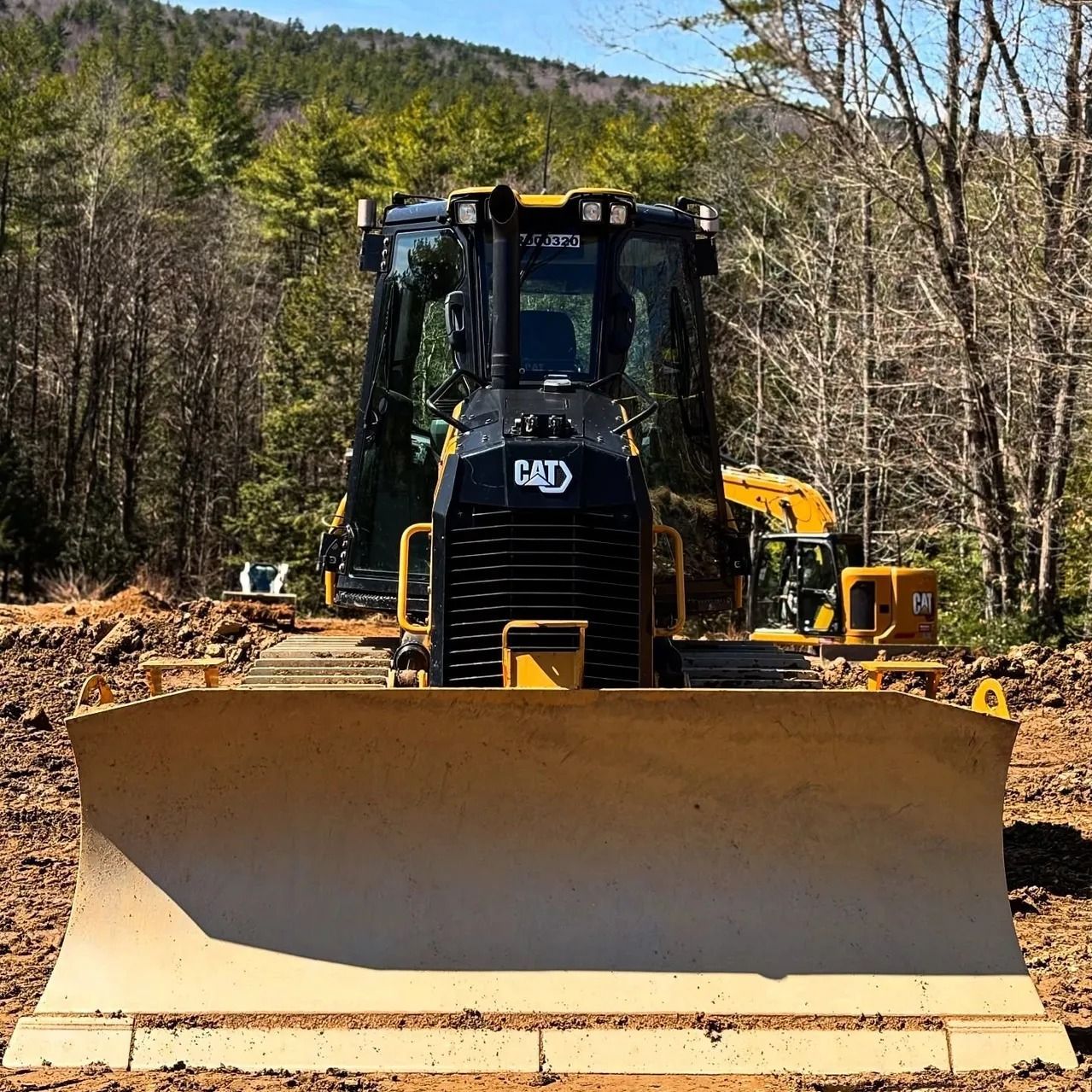 Yellow Caterpillar bulldozer on a dirt surface with a forest in the background.