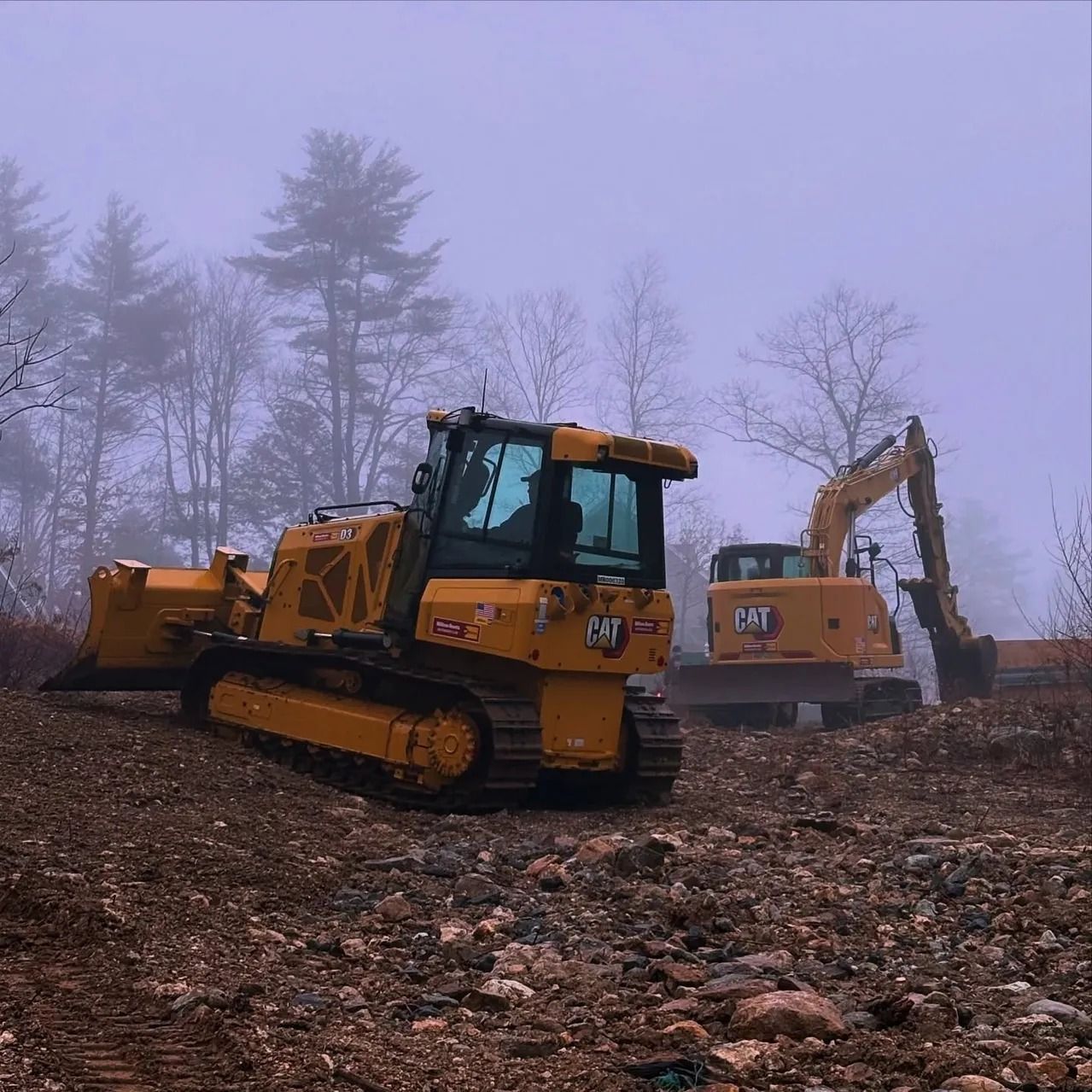 Yellow bulldozer and excavator on a construction site; trees in the background, foggy.