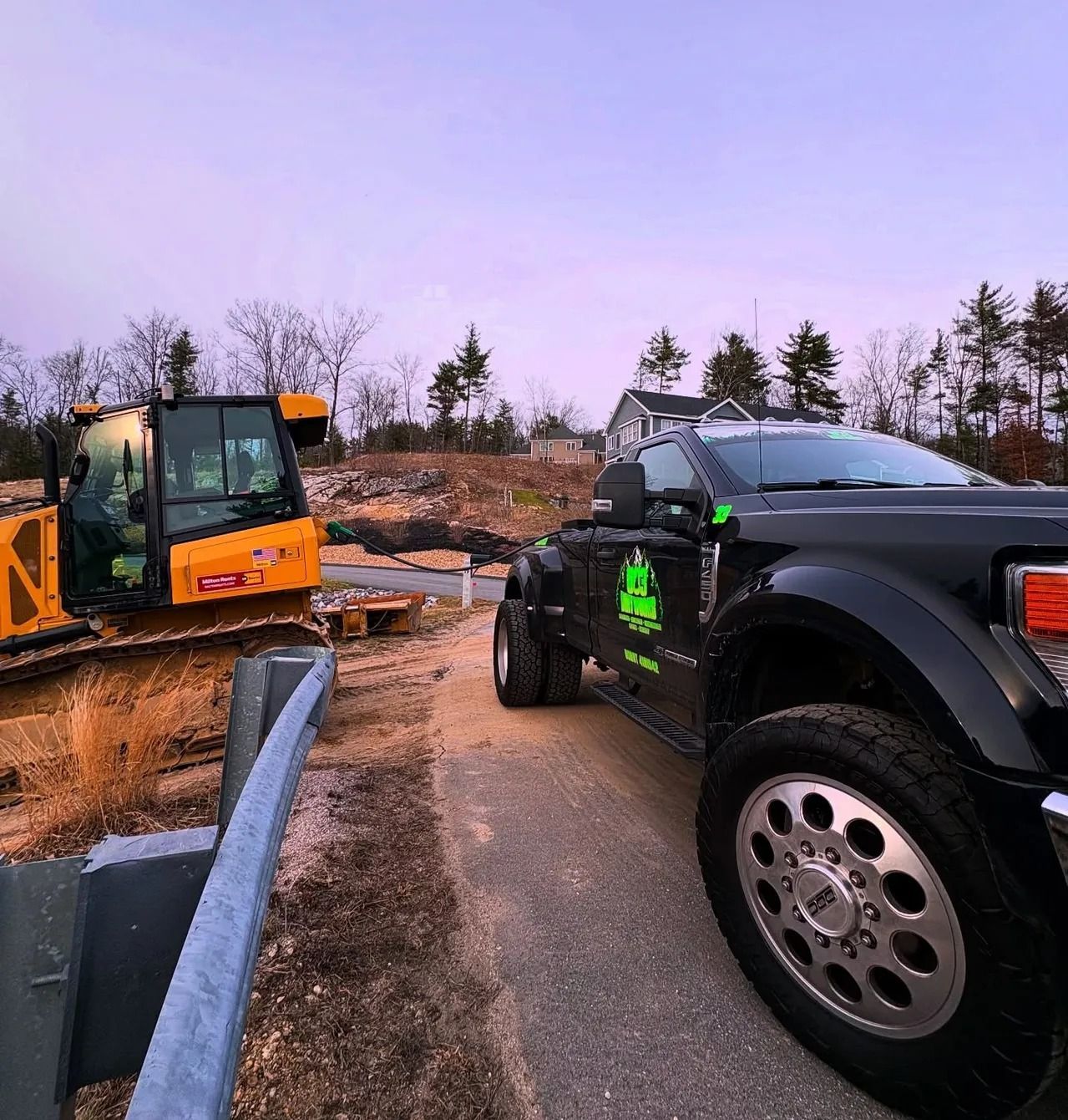 Black truck parked near a construction site with a yellow excavator. Gray sky, outdoor setting.