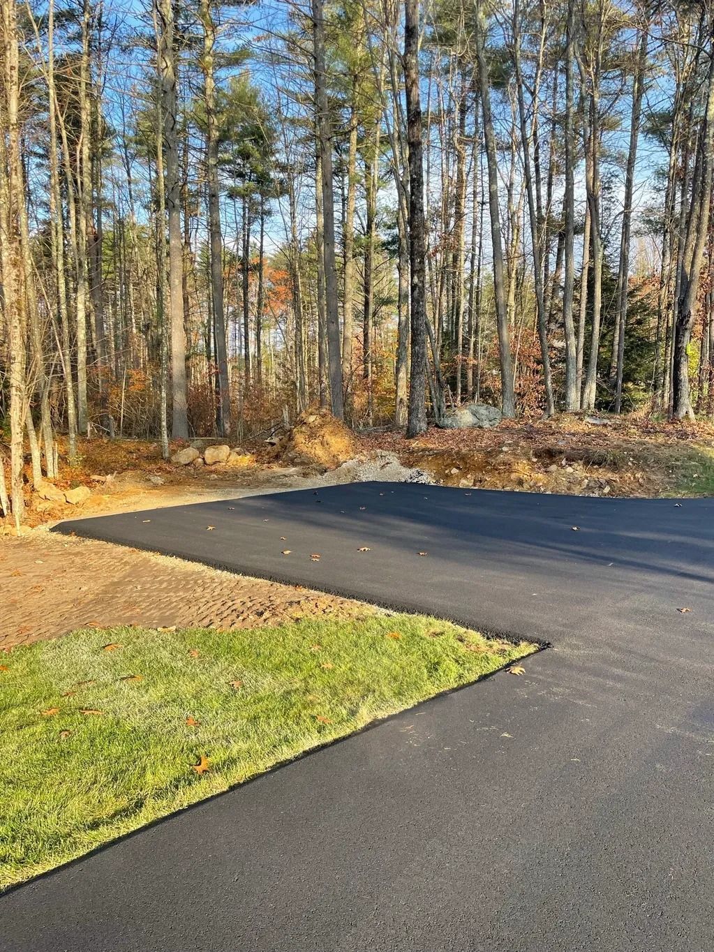 Newly paved asphalt driveway with a green lawn and a forest background.