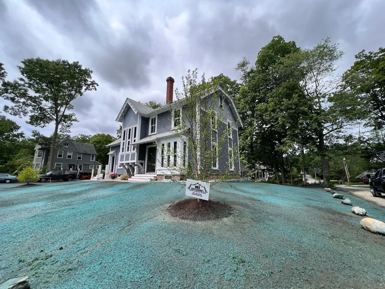 Gray house with white trim, green lawn, cloudy sky.
