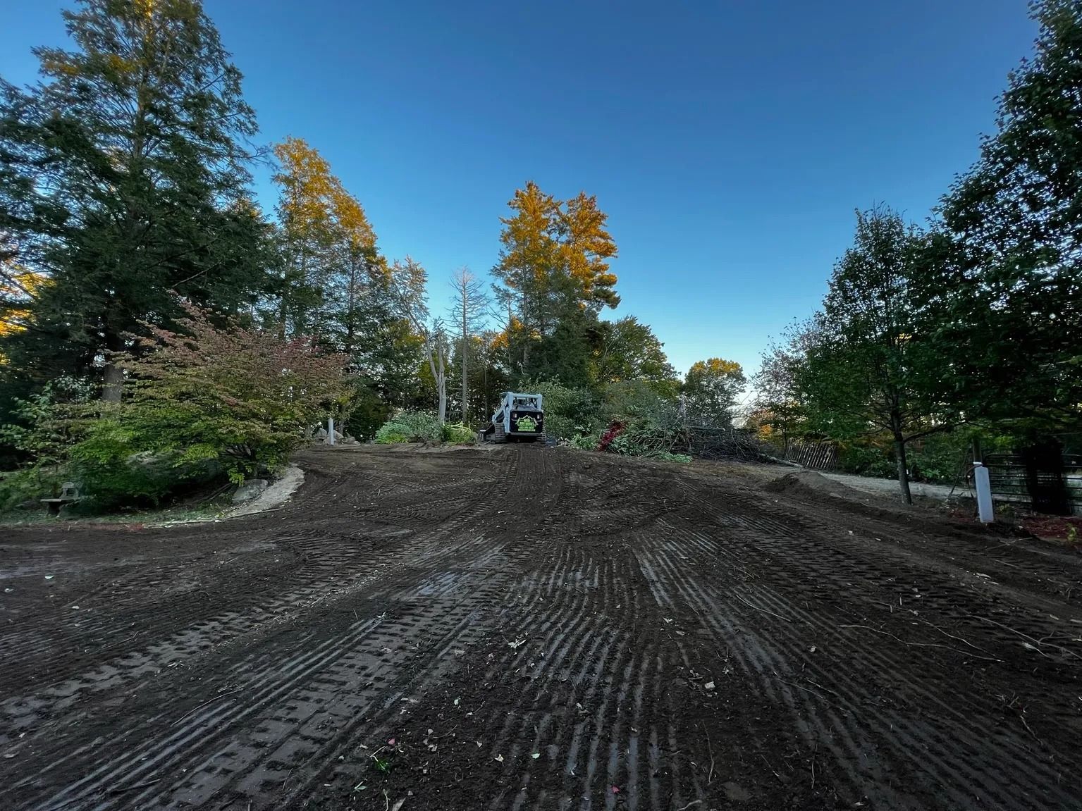A small bulldozer works on a dirt area with trees against a blue sky.