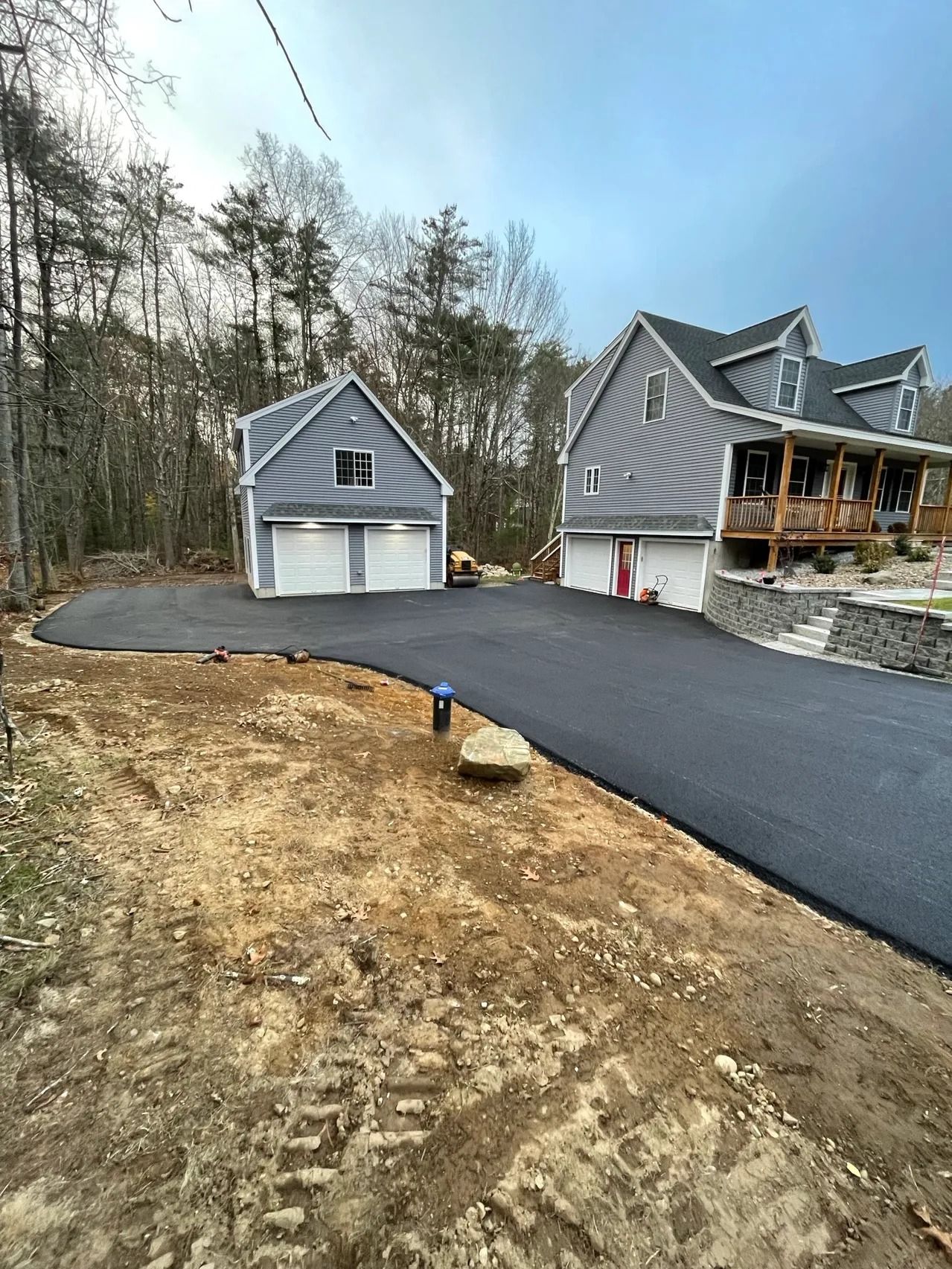 Newly paved driveway leading to a two-car garage and a multi-story house with a wooden porch.