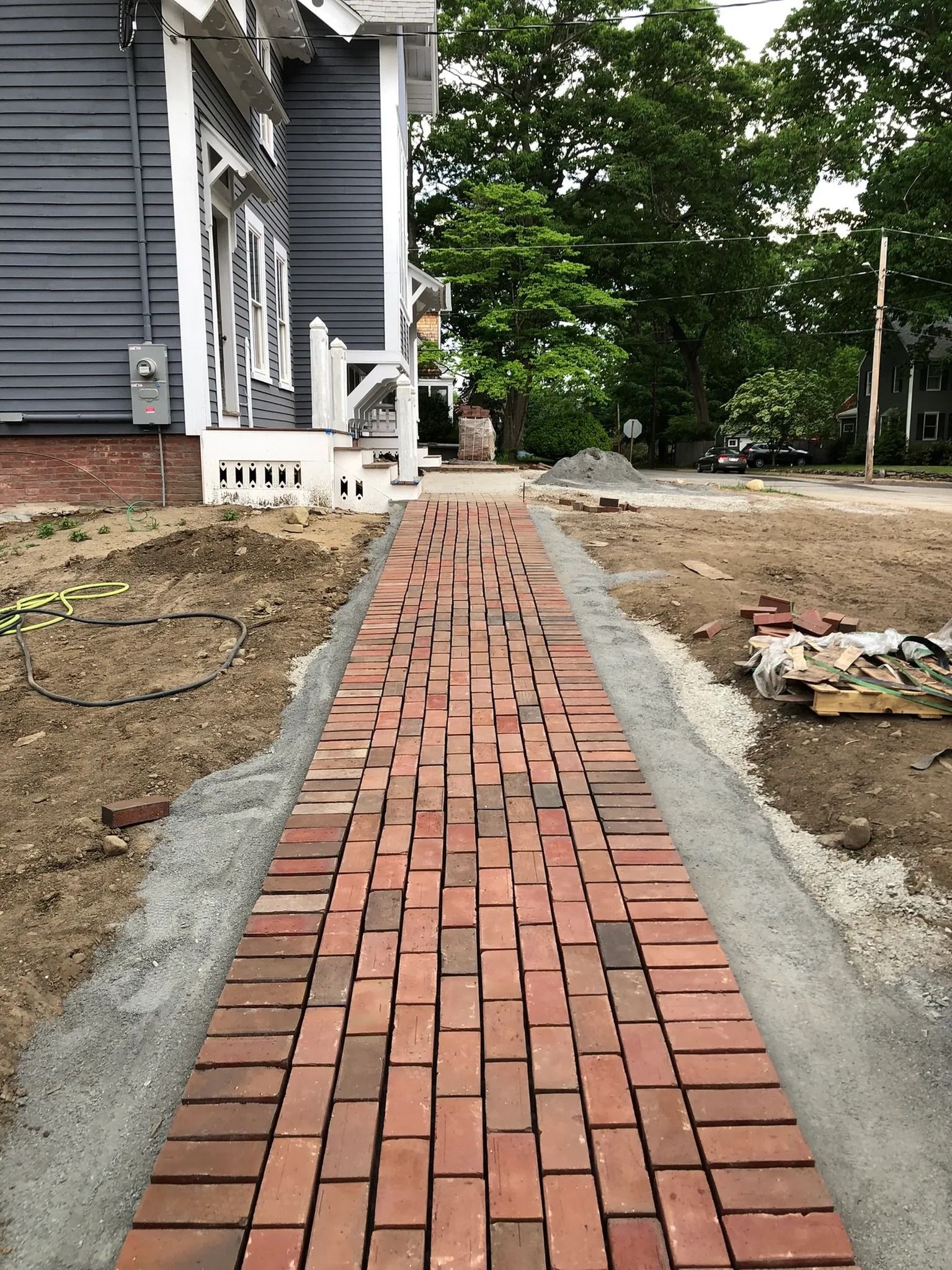 Brick walkway leading towards a building, with gray siding, and a gravel border.