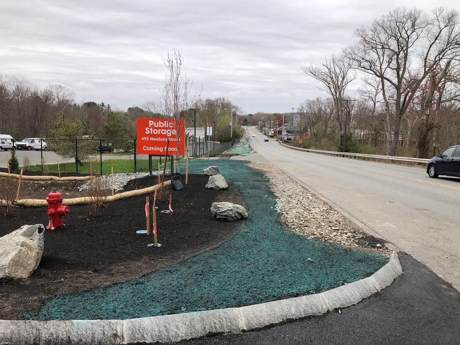 Roadside park with sign, landscaping, and a street. Cloudy sky overhead.