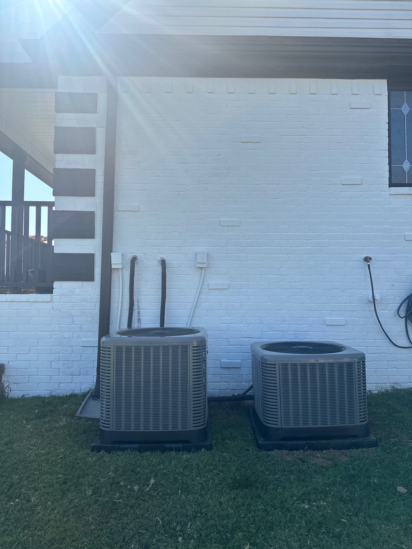 Two air conditioners are sitting on the side of a white brick building.