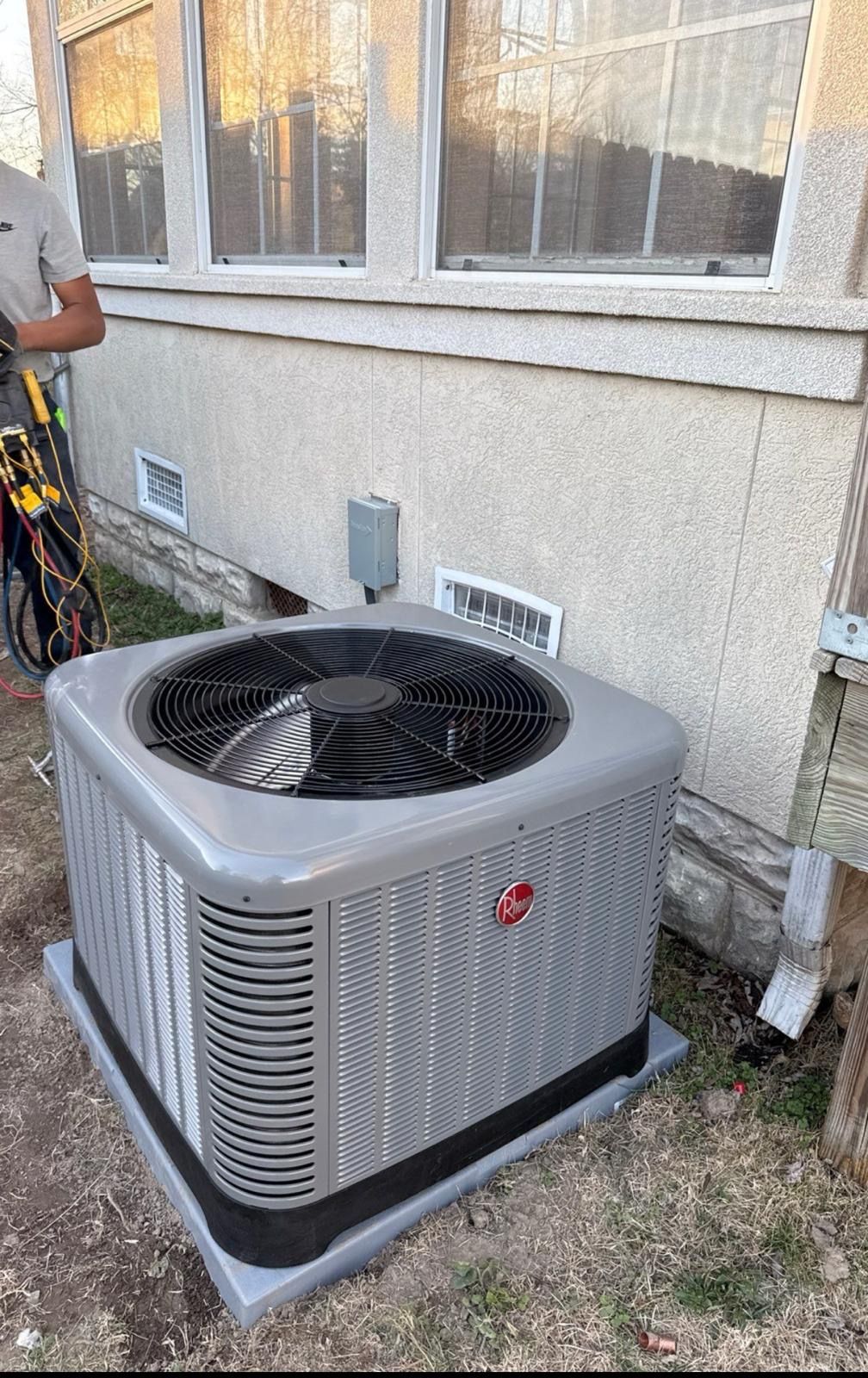 A man is working on an air conditioner outside of a house.