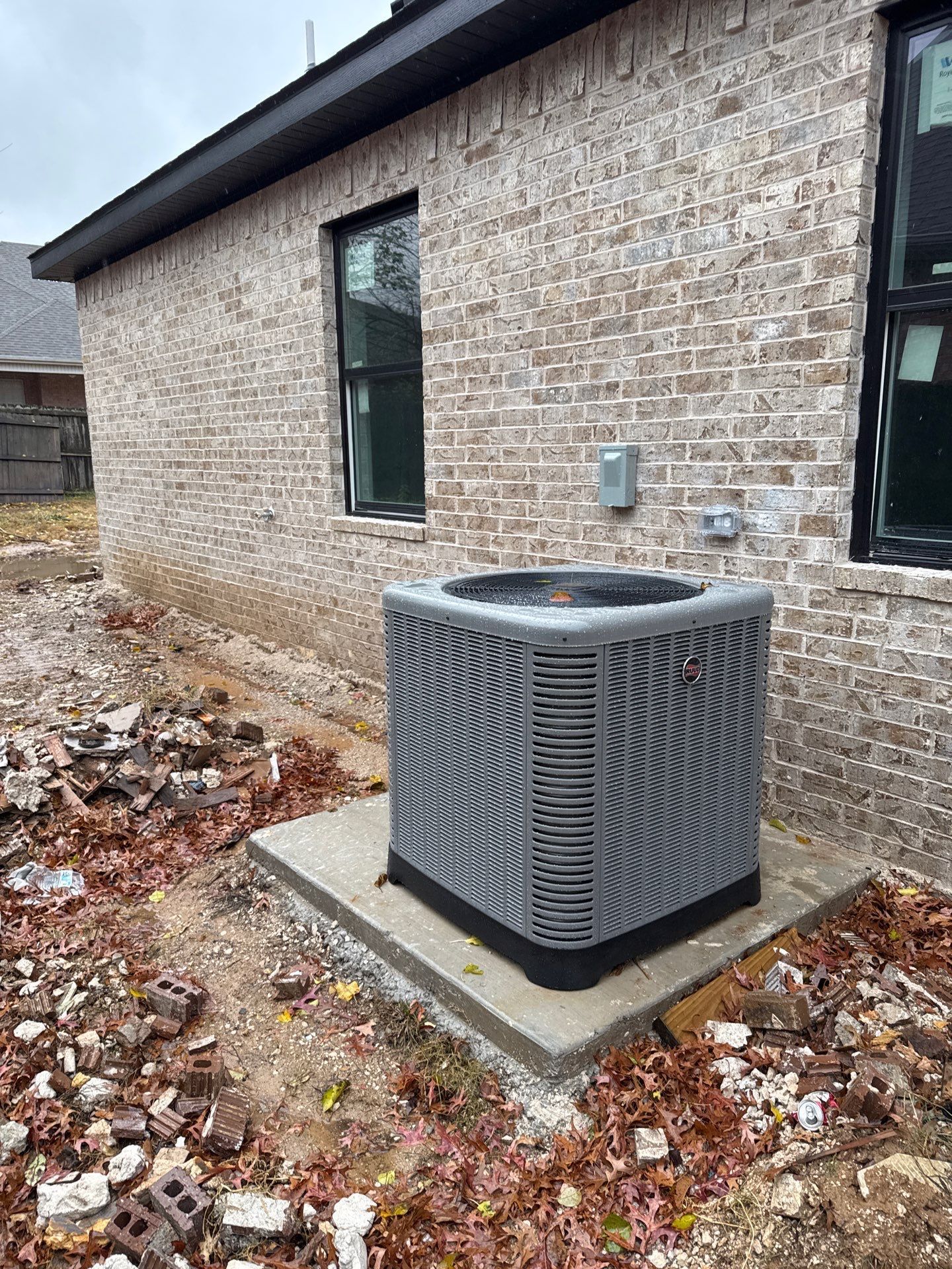 An air conditioner is sitting on the side of a brick house.