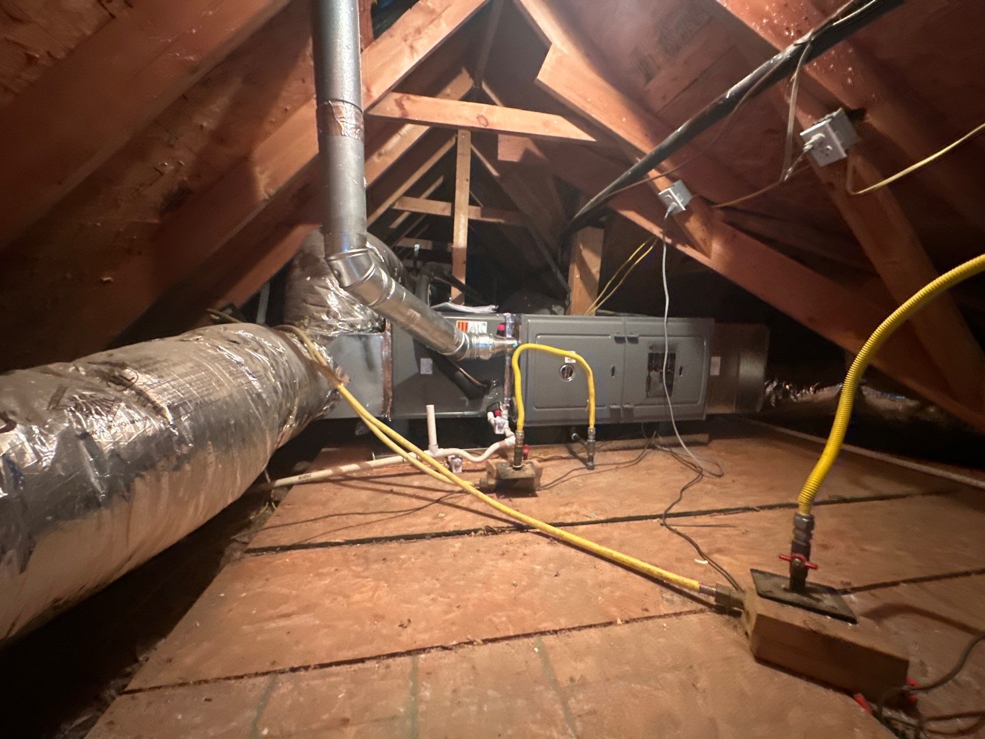 An attic with a lot of pipes and wires hanging from the ceiling.