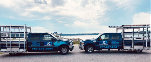 Two blue utility trucks facing each other on a roadside, with flatbed trailers and water in the background