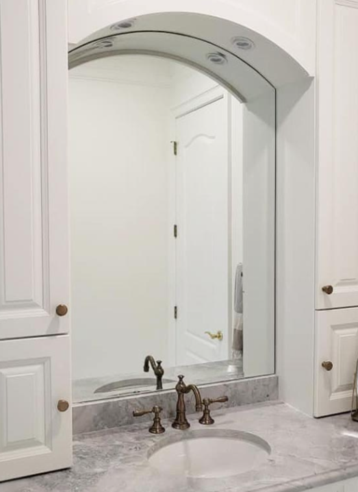 Bathroom vanity with curved mirror, marble countertop, sink, and cabinet storage
