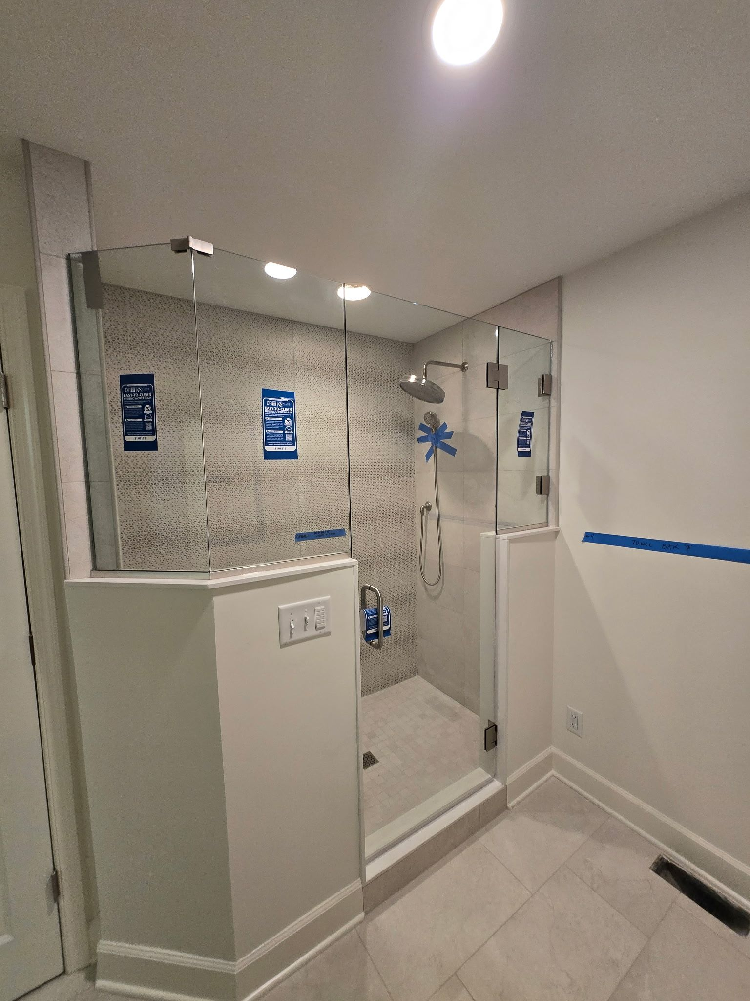 Accessible shower stall with grab bars, white tile, and fold-down seat in a bright bathroom