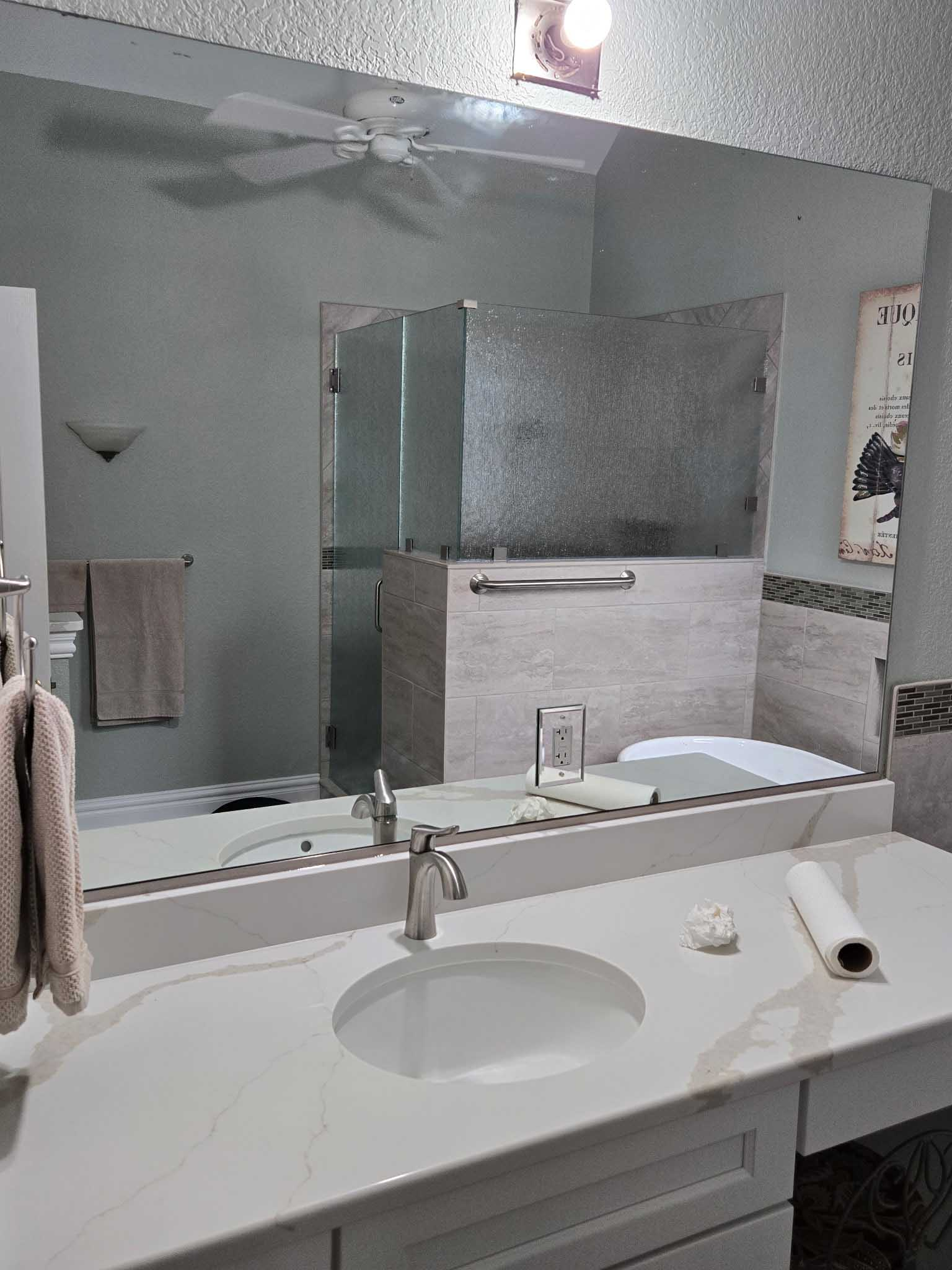 A modern bathroom vanity with a white marble countertop, an under-mount sink, chrome faucet, and a large mirror.