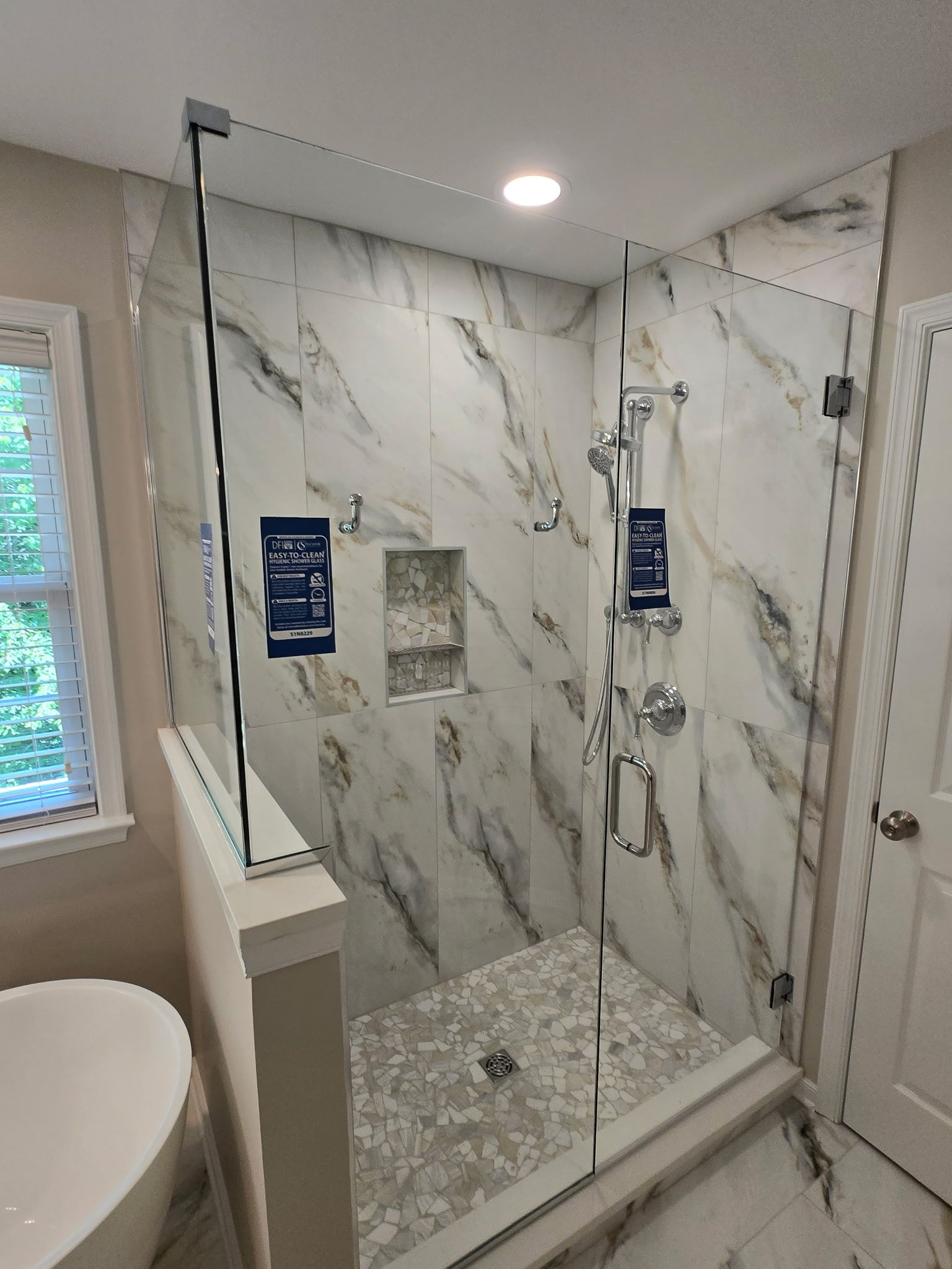 Modern marble-tile walk-in shower with glass door, chrome fixtures, and recessed ceiling light.